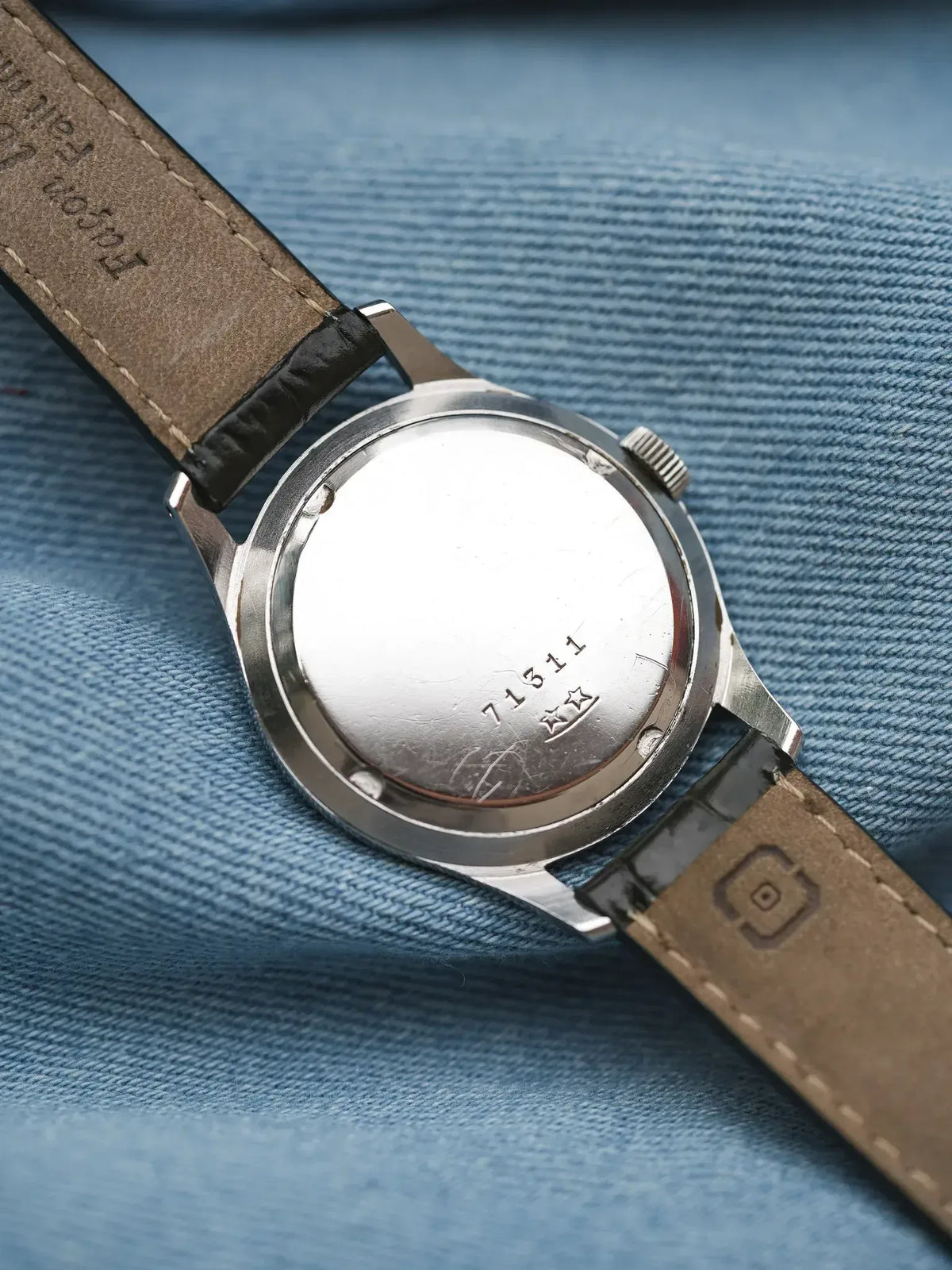 Vintage Omega watch back with engraved serial number, steel case, brown leather strap on denim
