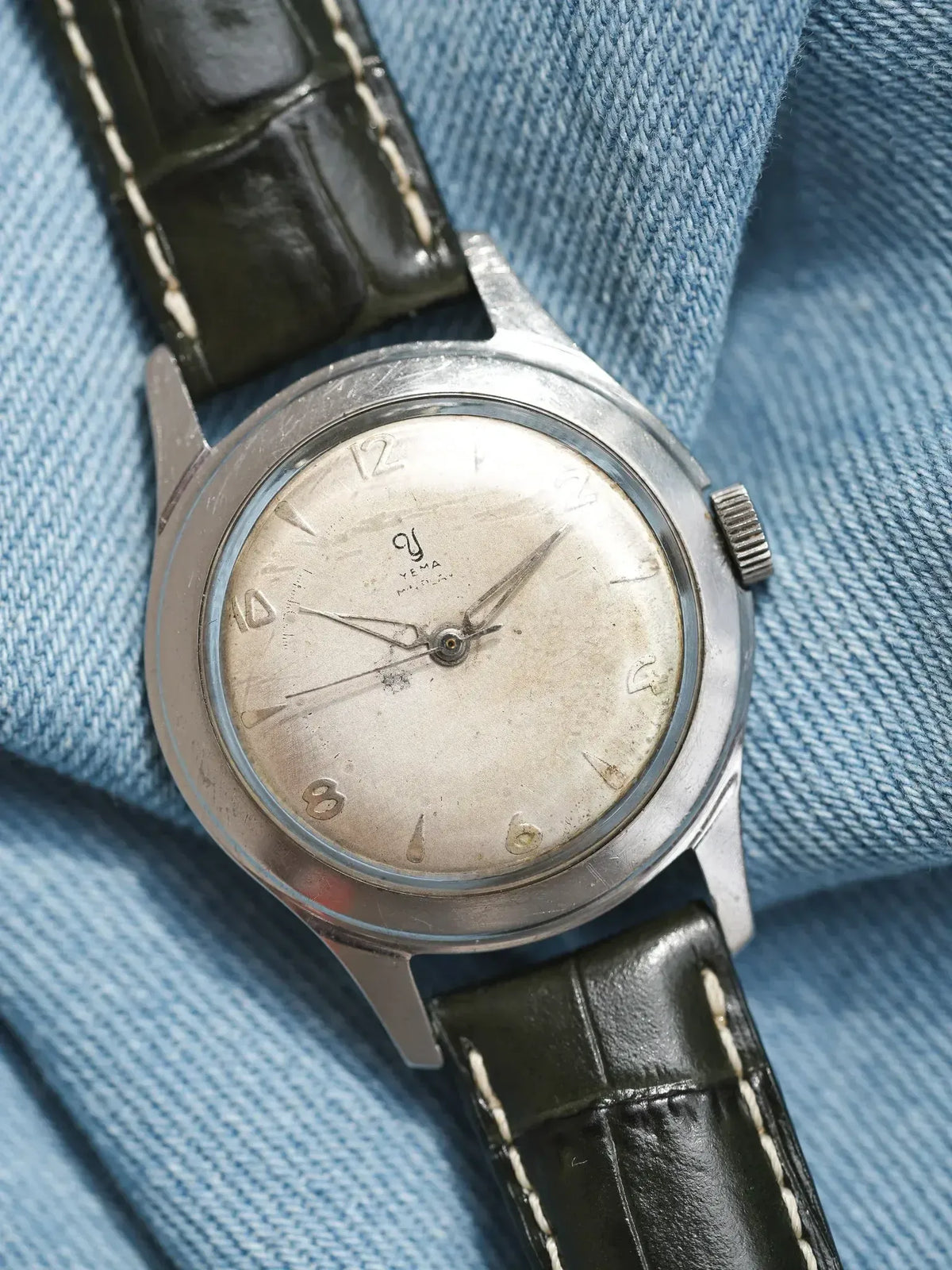 Vintage Yema wristwatch with silver dial, black leather strap, on denim background