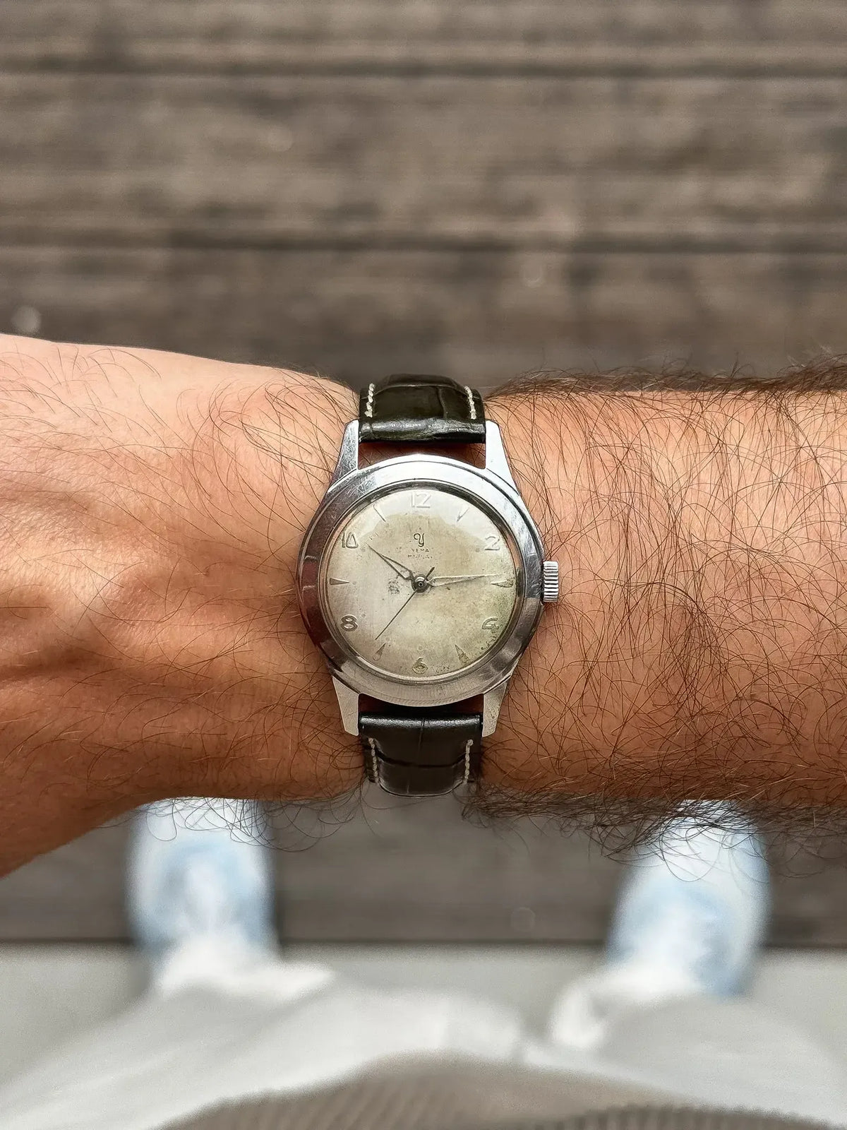 Vintage Omega wristwatch with silver dial, black leather strap, worn on hairy wrist