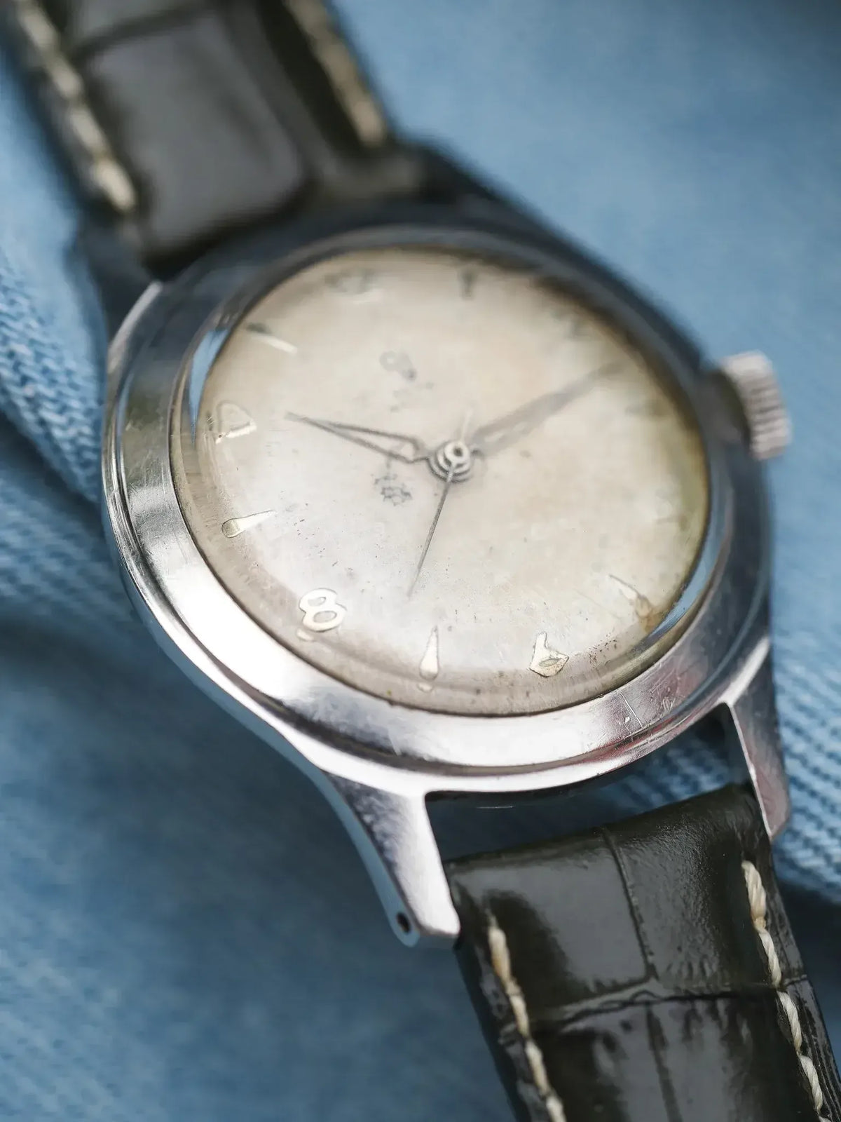 Vintage Omega watch with silver dial, black leather strap, on denim background