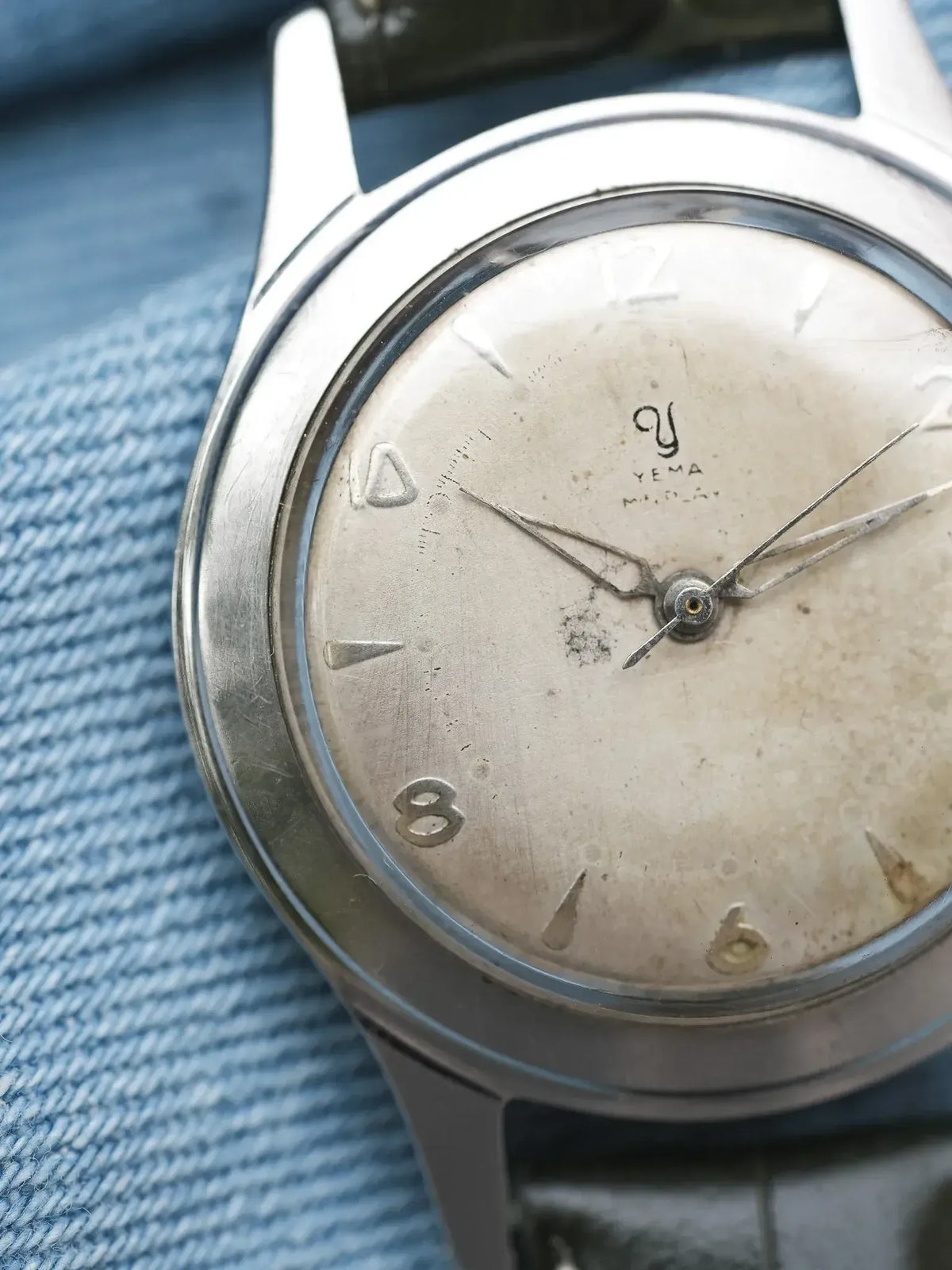 Vintage Yema wristwatch with aged silver dial, steel case, resting on denim fabric