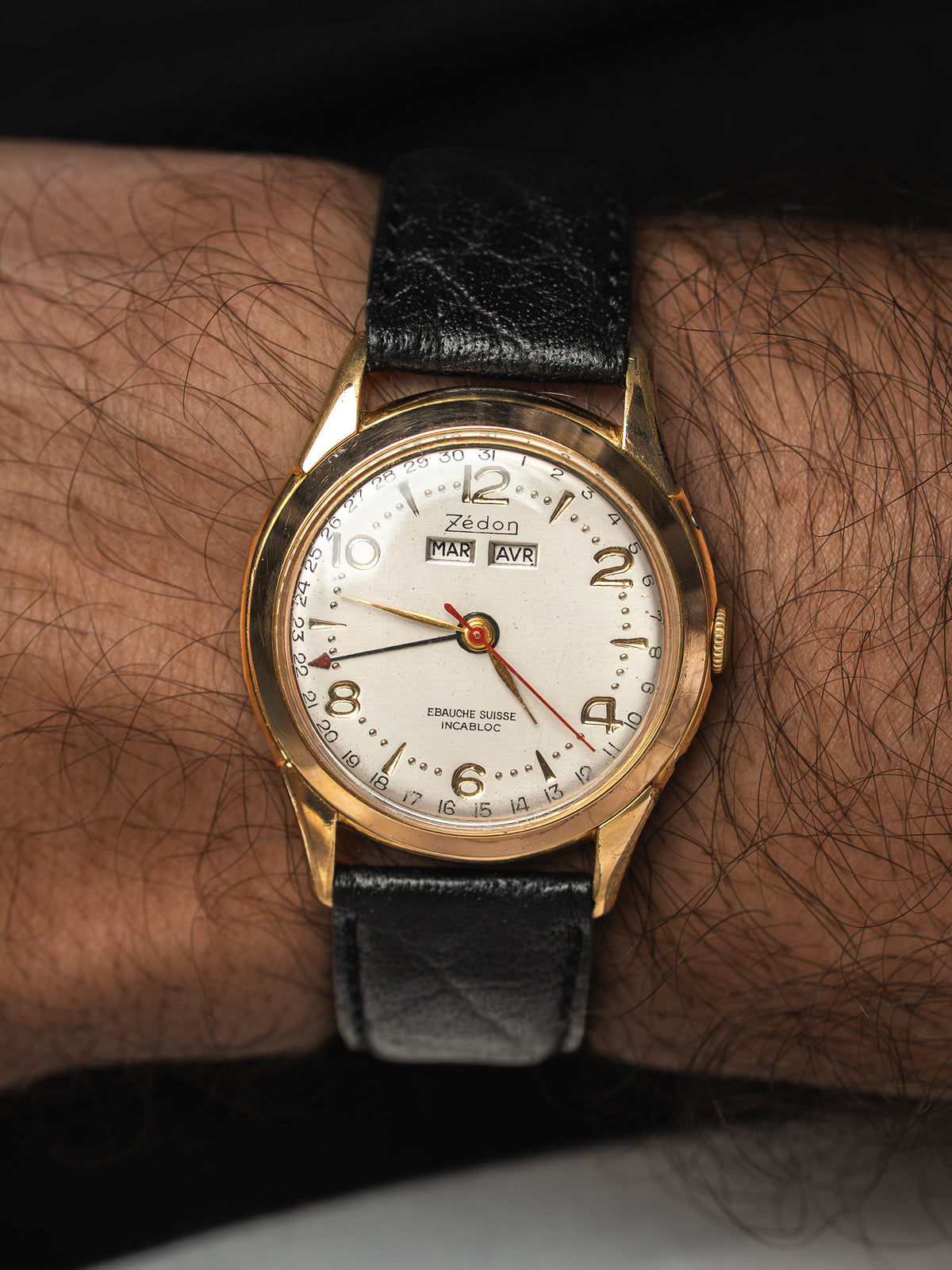Montre Zédon vintage, boîtier doré, cadran blanc et bracelet cuir noir au poignet