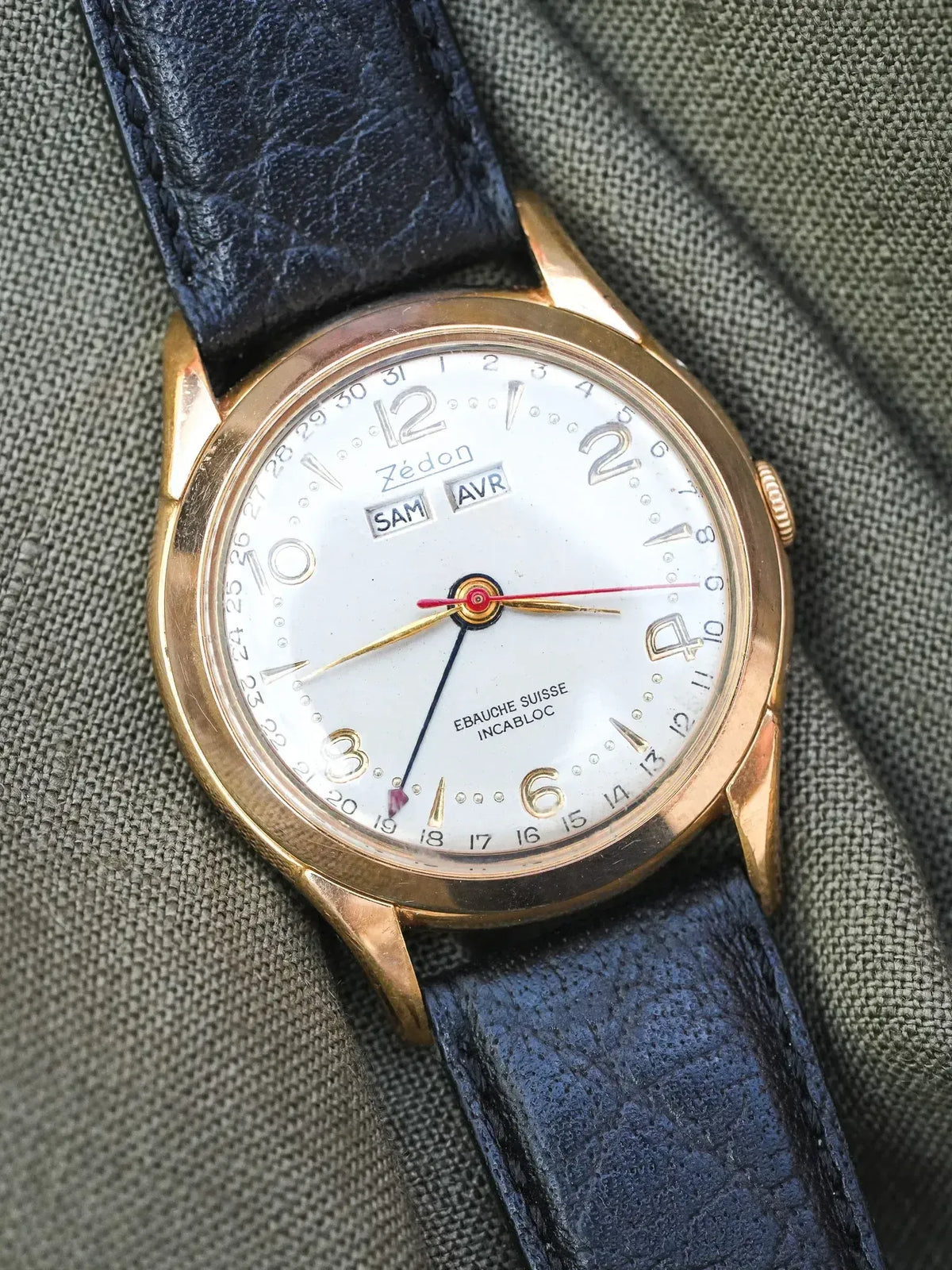 Zédon vintage watch with gold case, white dial, blue leather strap on fabric