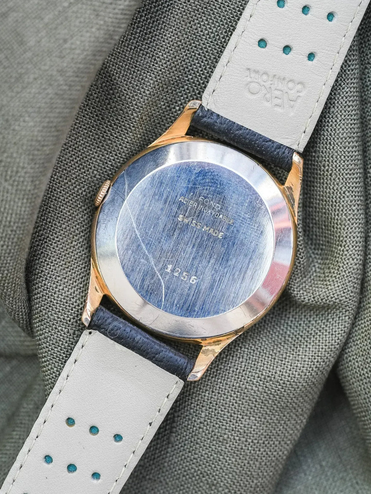 Vintage Universal Genève watch with gold case, stainless steel back, and white leather strap