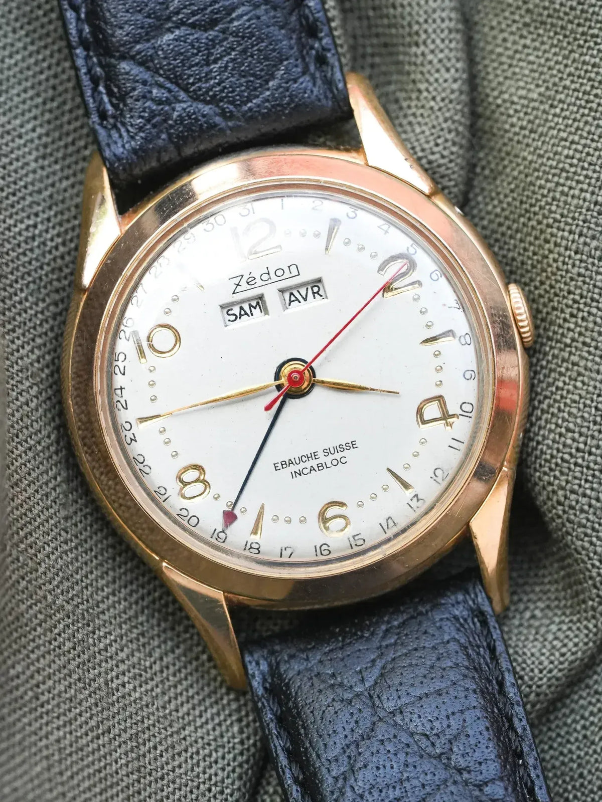Zédon vintage watch with gold case, white dial, blue leather strap on fabric
