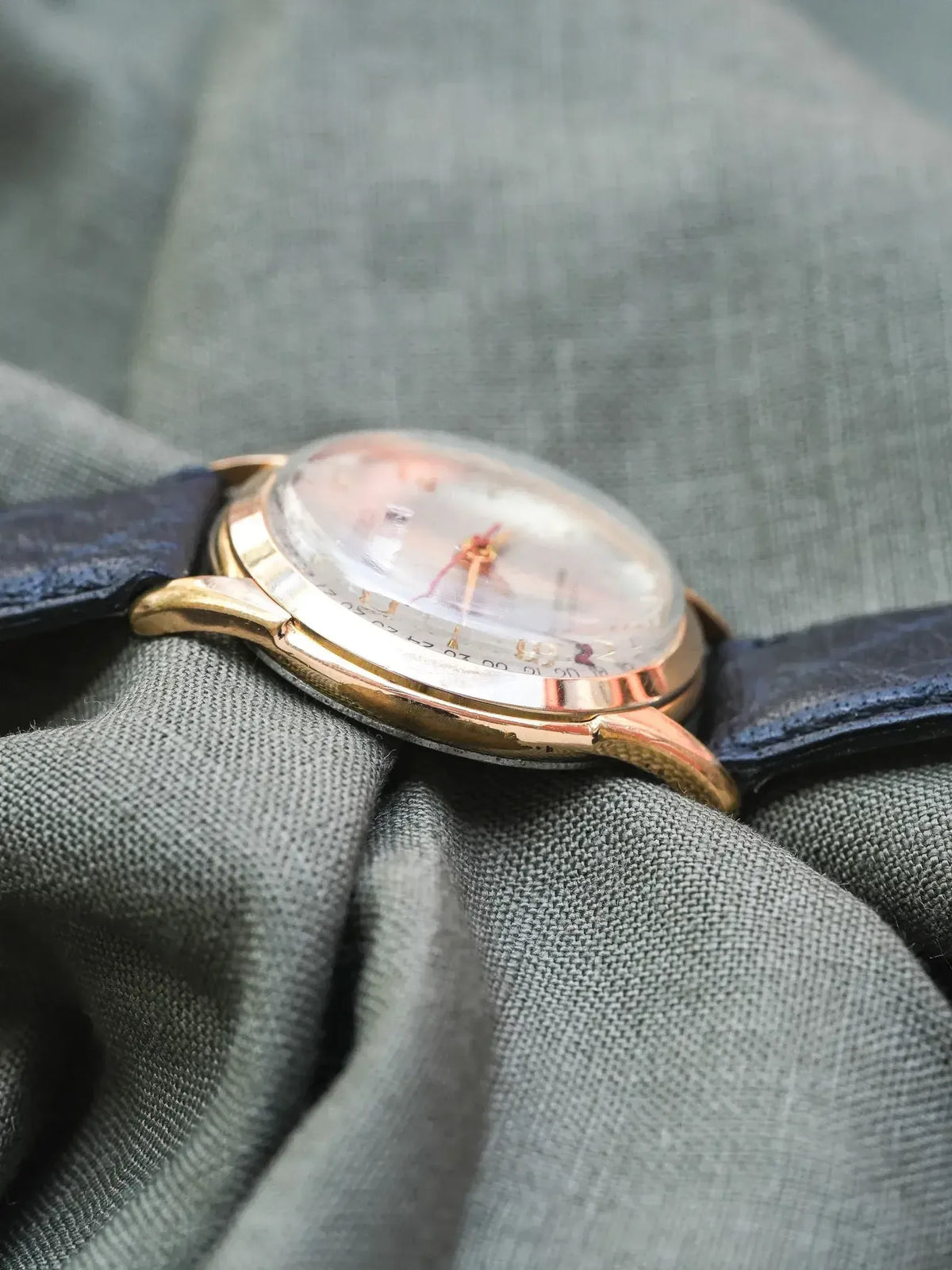 Vintage Universal Genève watch with gold case, silver dial, and dark leather strap on fabric