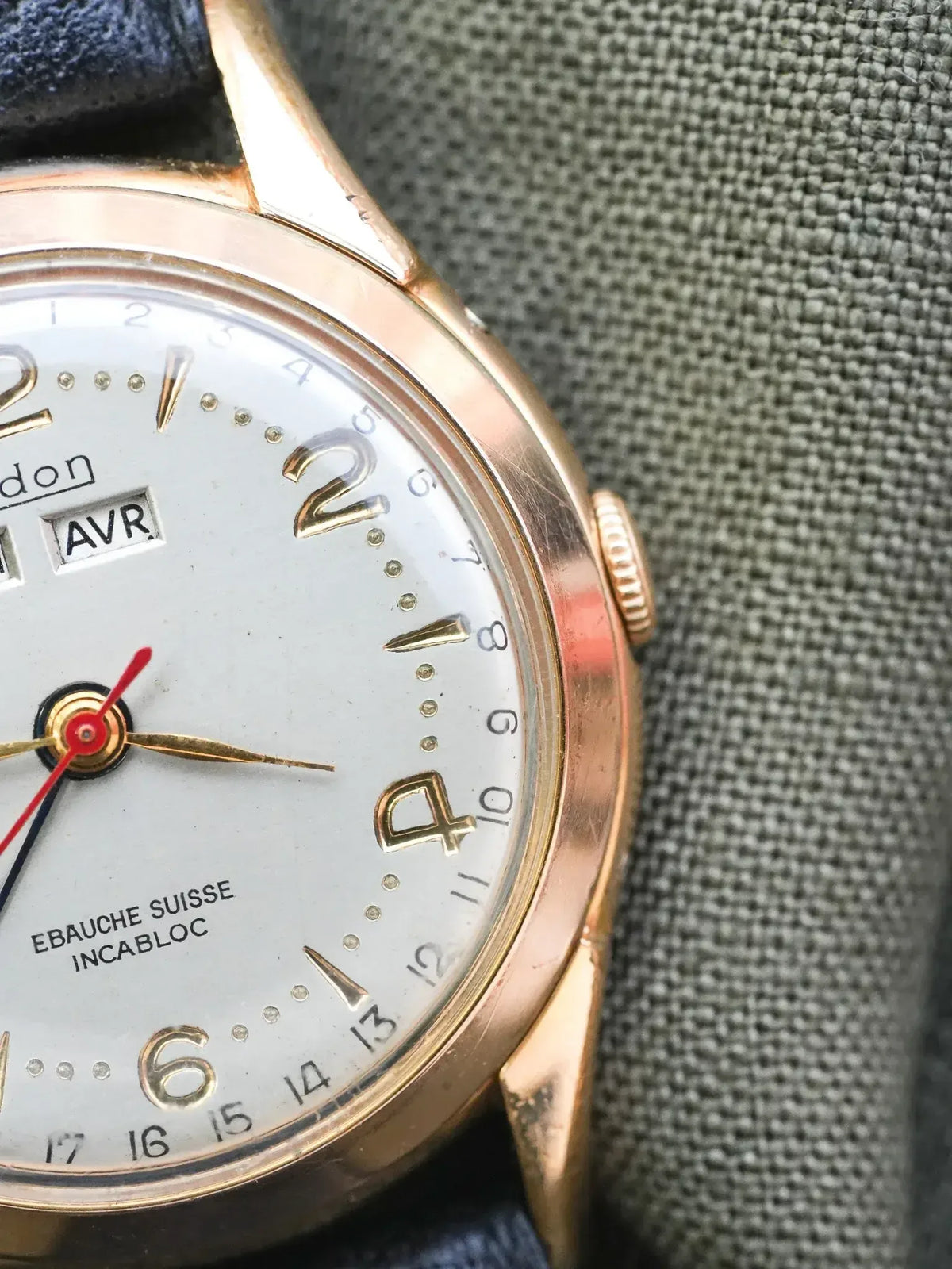 Vintage Longines watch with gold case, silver dial, and blue leather strap on textured background