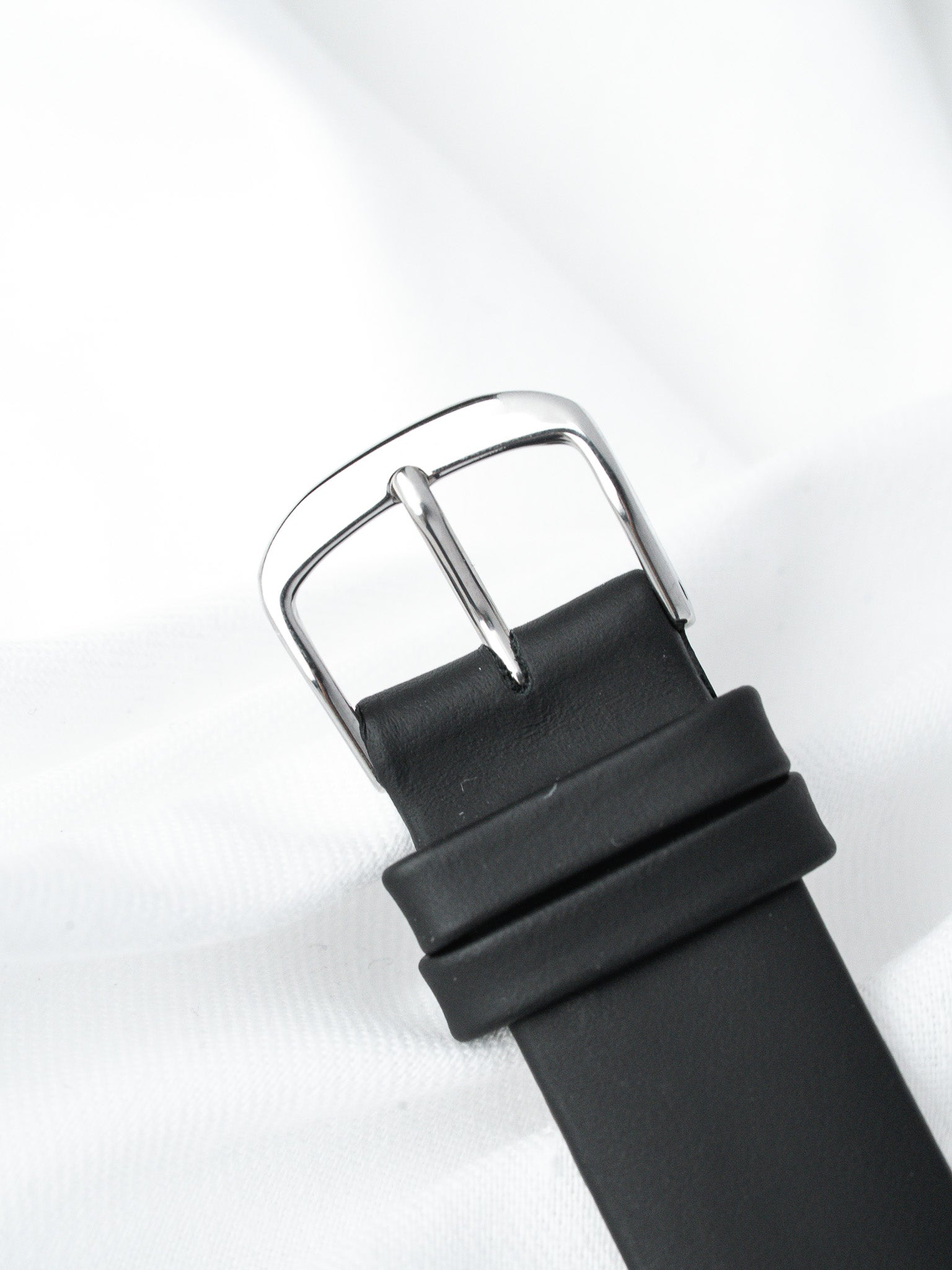 Black leather watch strap with polished steel buckle on white background