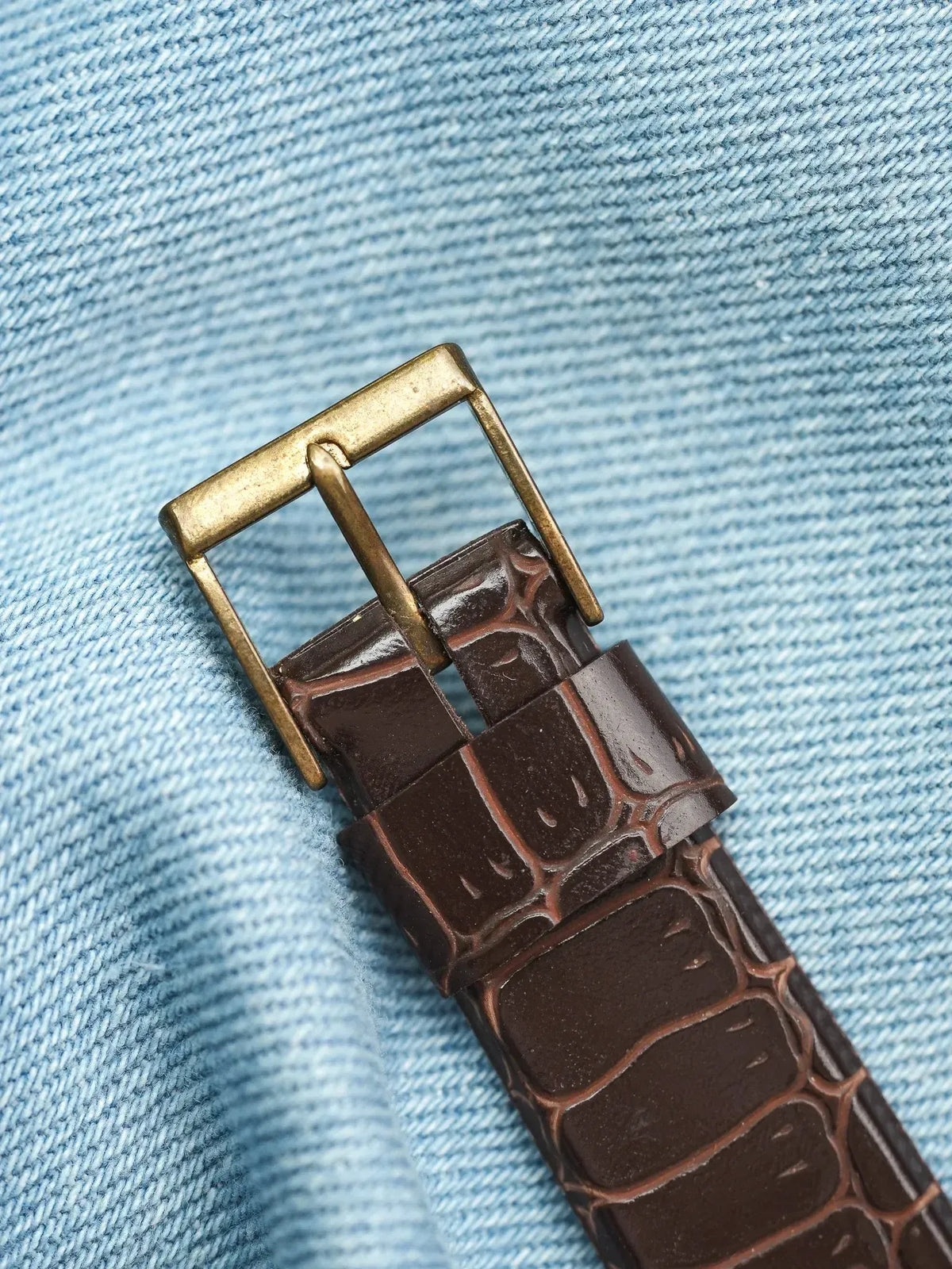 Brown alligator leather watch strap with brass buckle on denim background