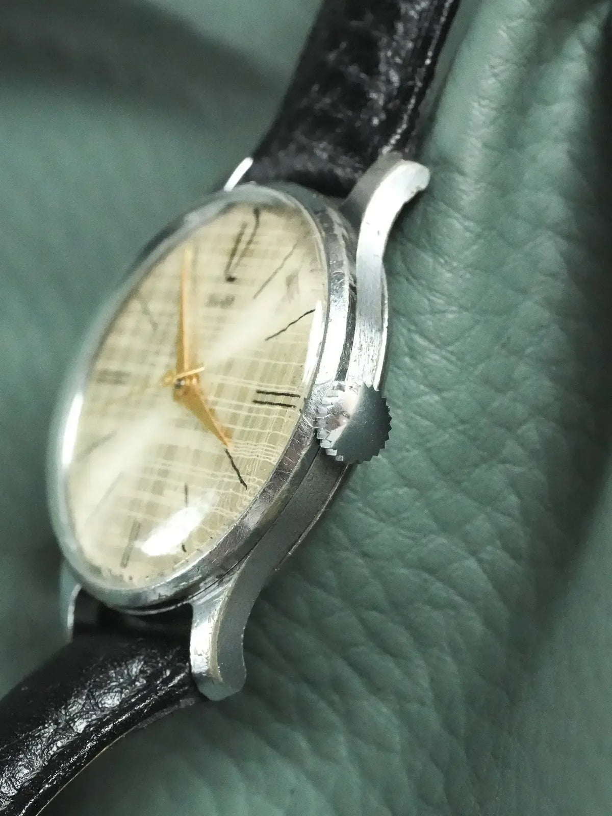 Vintage Universal Genève watch with silver case, cream checkered dial, black leather strap on green leather