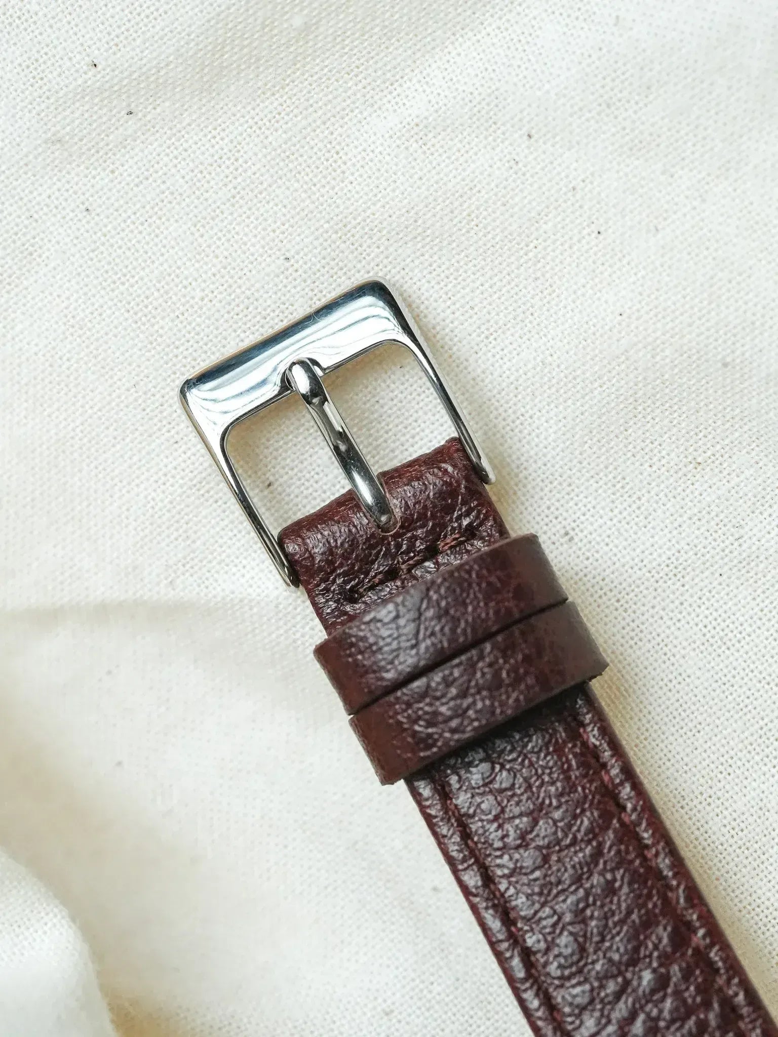 Vintage leather watch strap with silver buckle, burgundy textured finish on canvas