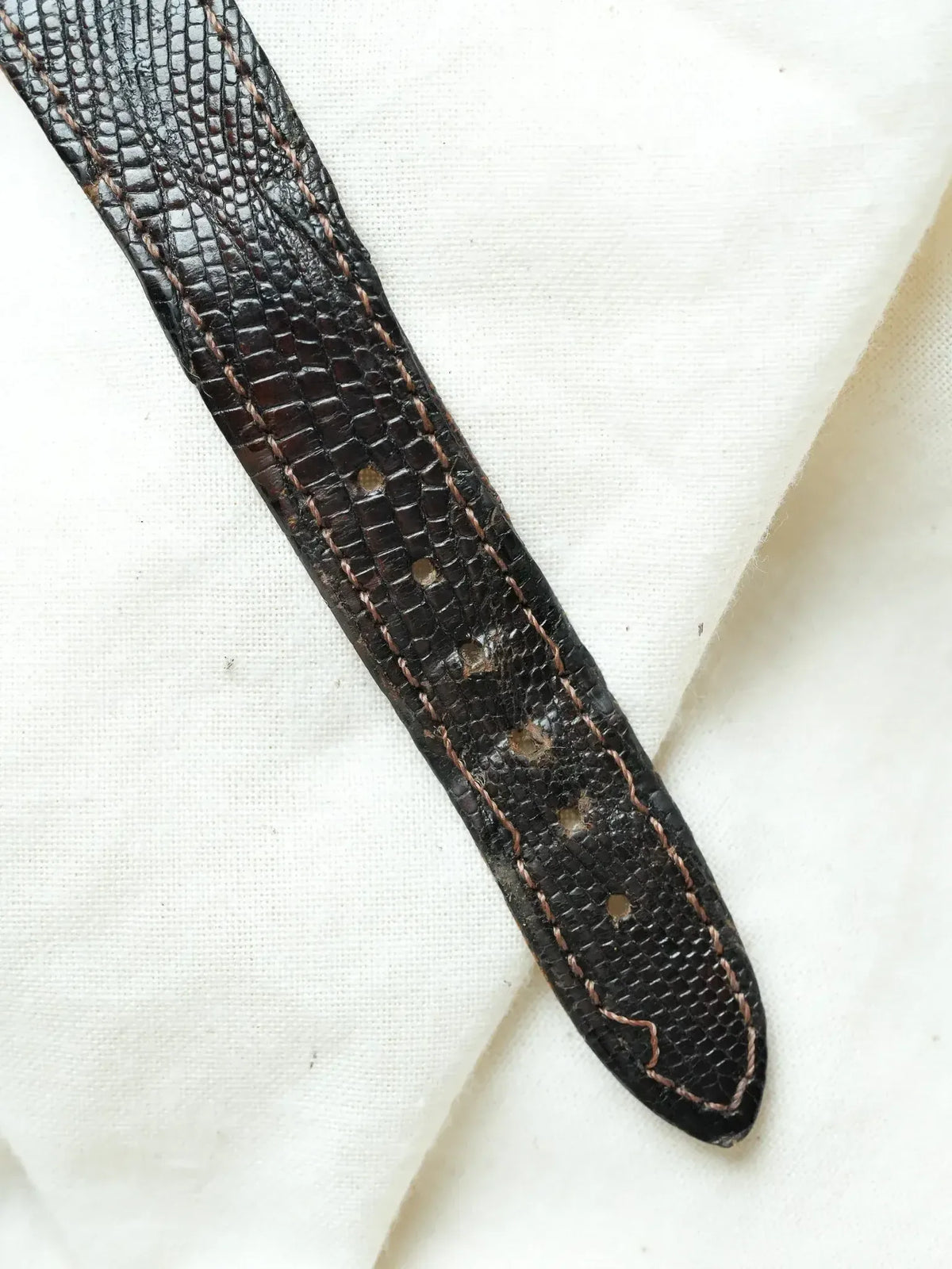 Vintage watch strap in black lizard skin with brown stitching on white fabric