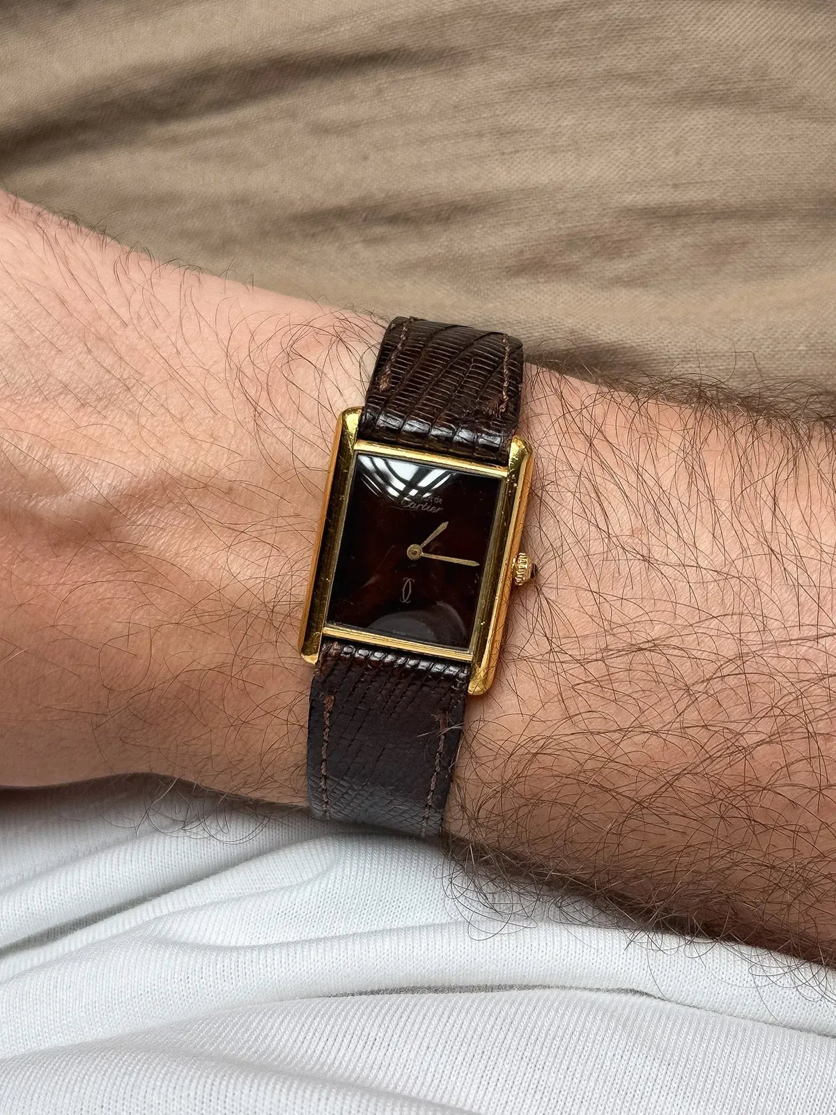 Cartier Tank vintage watch with gold case, dark dial, brown leather strap on wrist