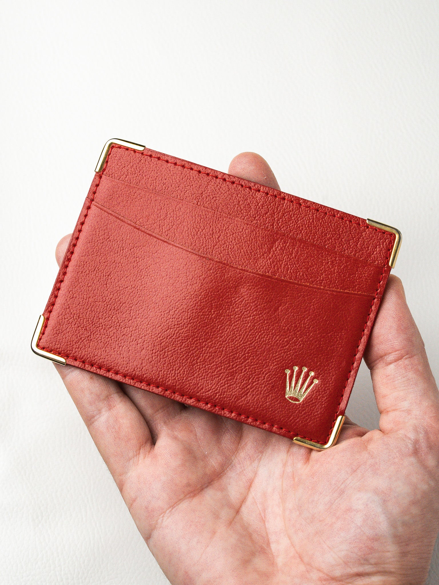 Red leather cardholder with gold Rolex crown logo, held in hand