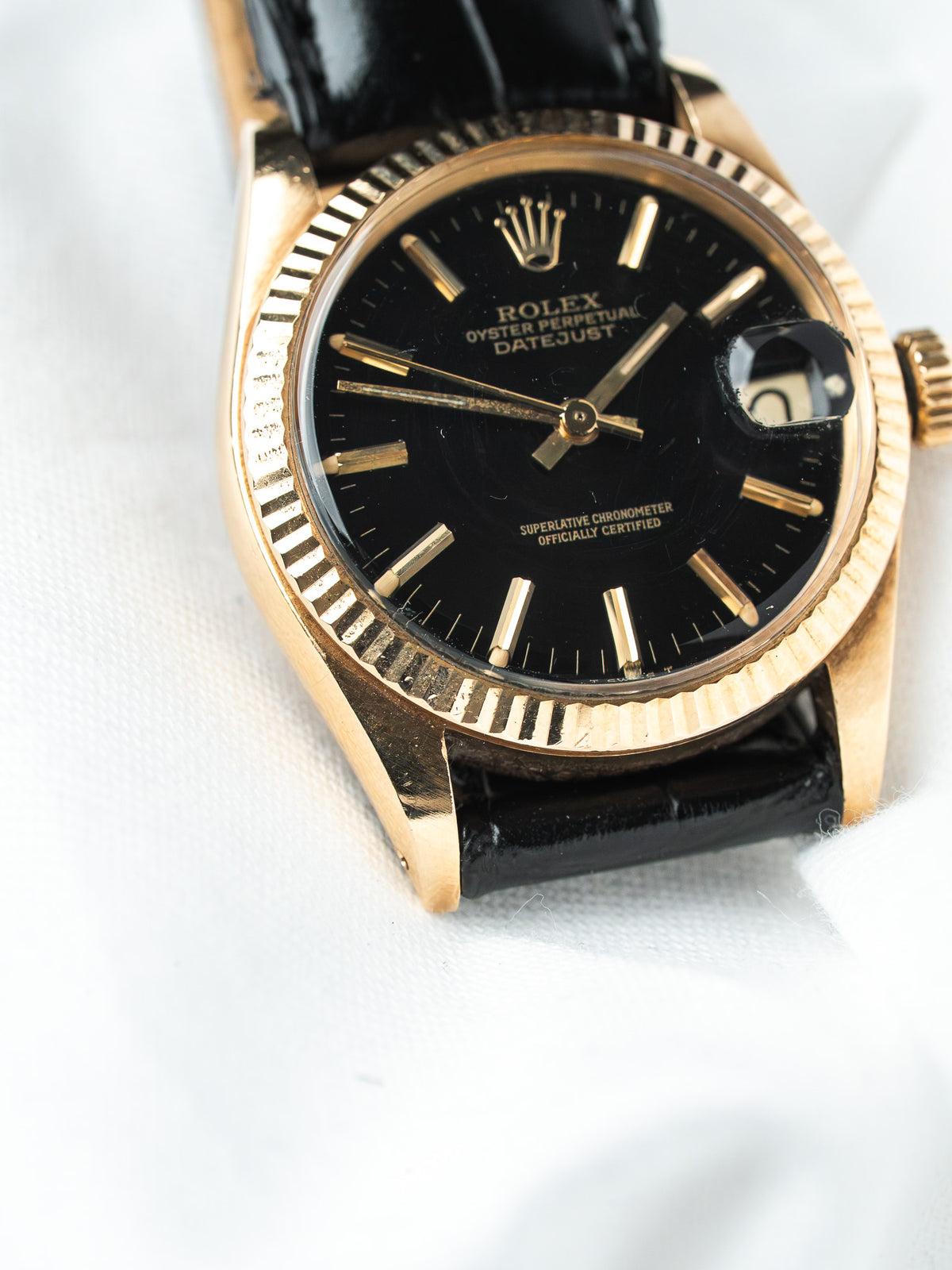 Vintage Rolex Datejust with black dial, gold bezel, and black leather strap on white background