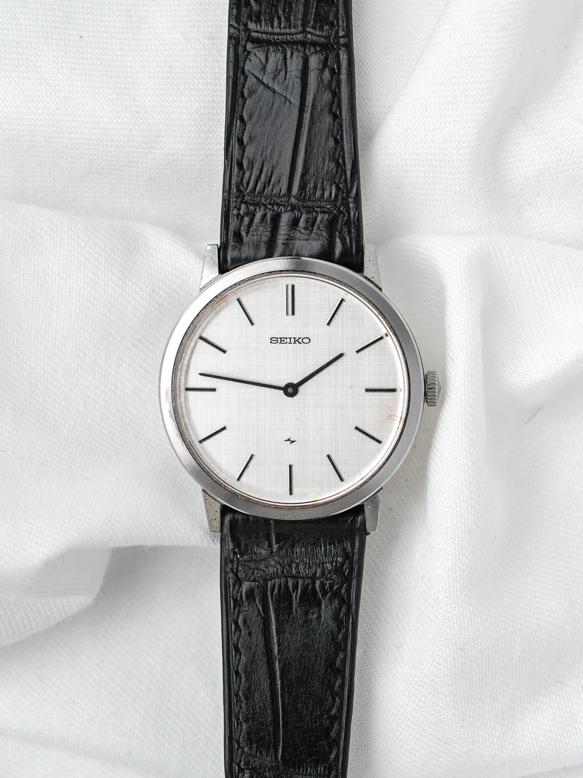 Seiko vintage watch with silver dial, black leather strap, on white fabric