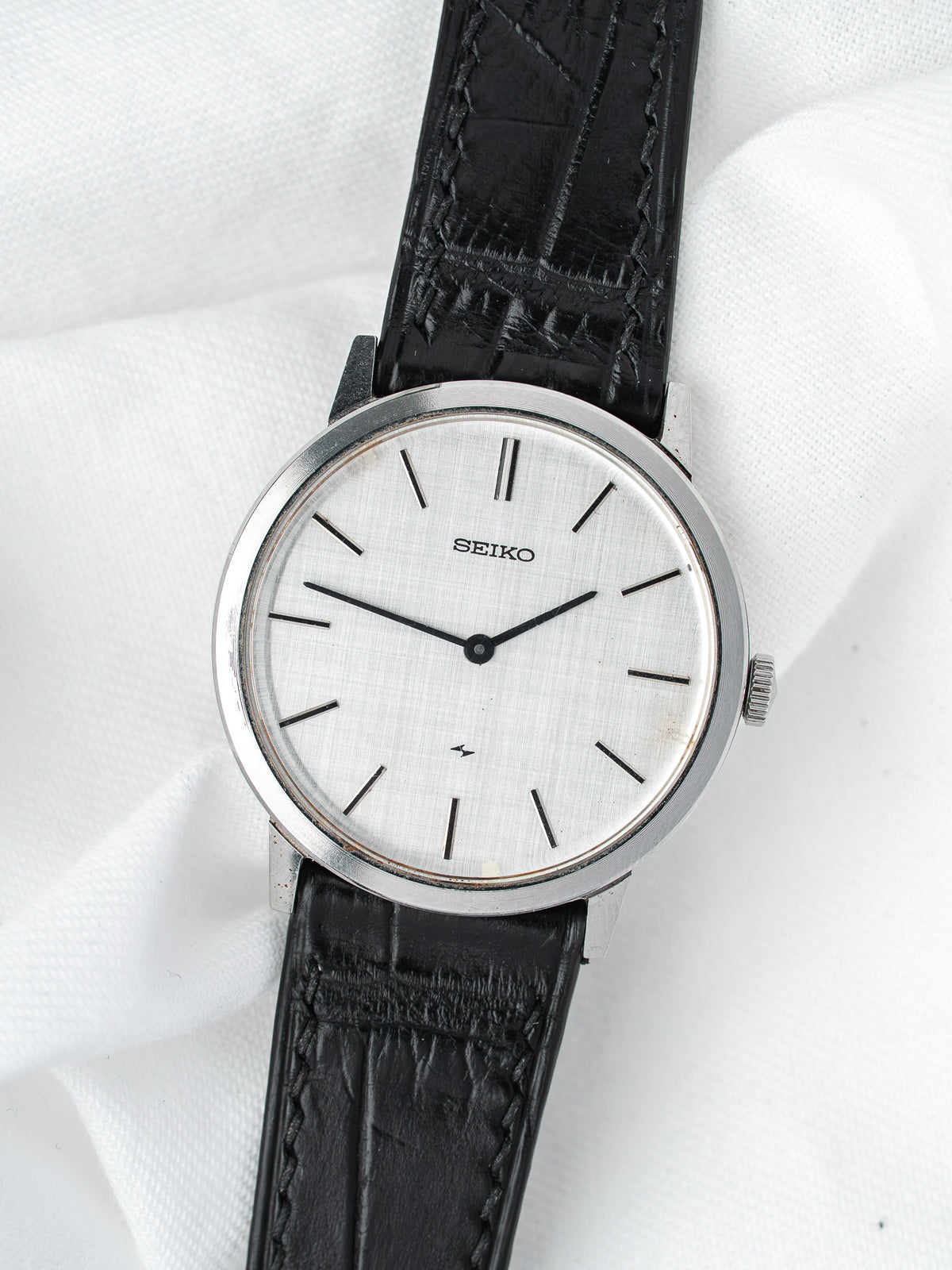 Seiko vintage watch with silver dial, black leather strap, and steel case on white fabric
