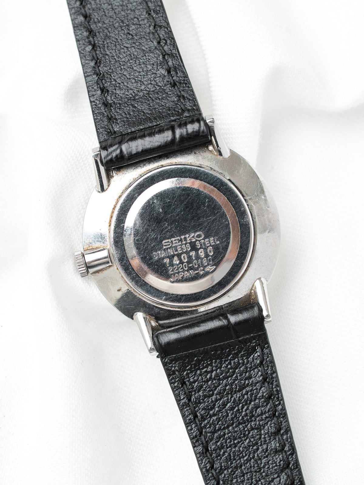 Vintage Seiko watch with stainless steel case, black leather strap, back view on white background