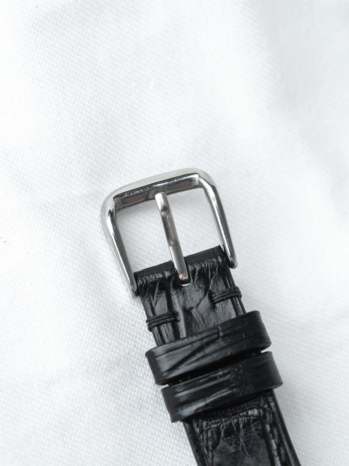Black leather watch strap with silver buckle on white background