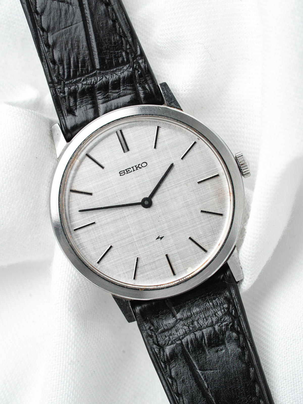 Seiko vintage watch with silver dial, black leather strap, on white fabric