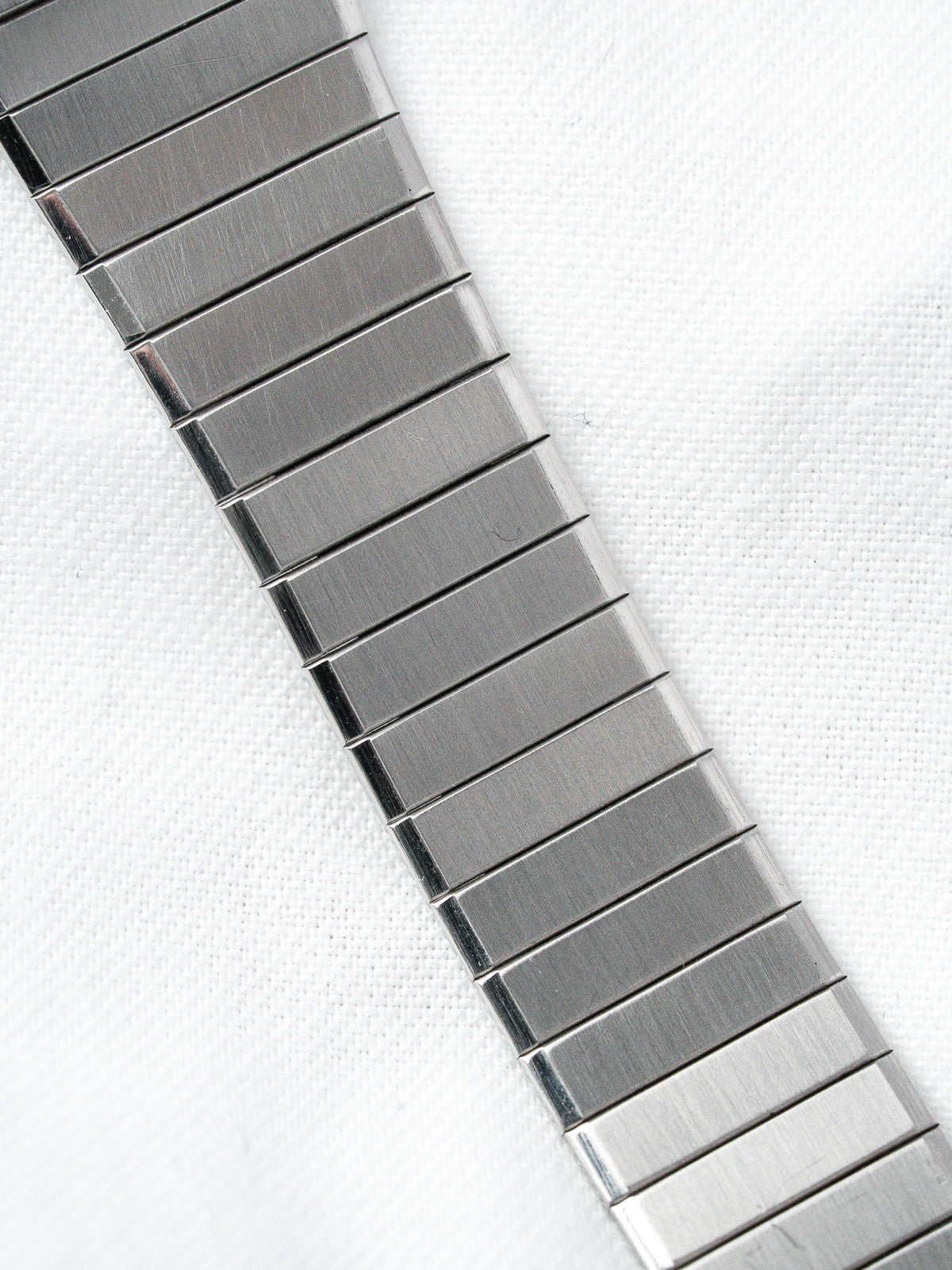 Stainless steel watch bracelet with brushed finish, laid on white textured fabric