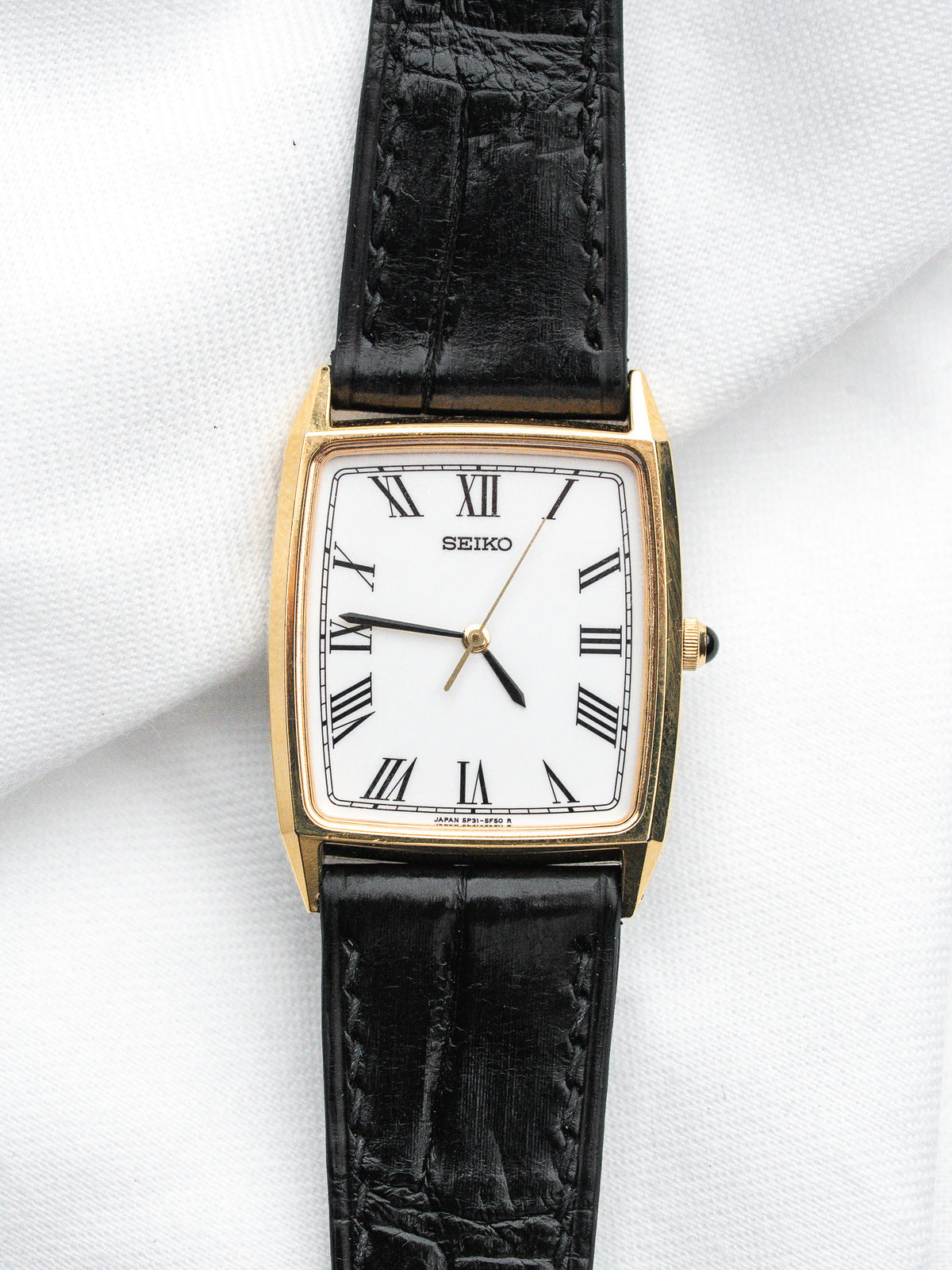 Seiko vintage watch with gold case, white dial, Roman numerals, black leather strap