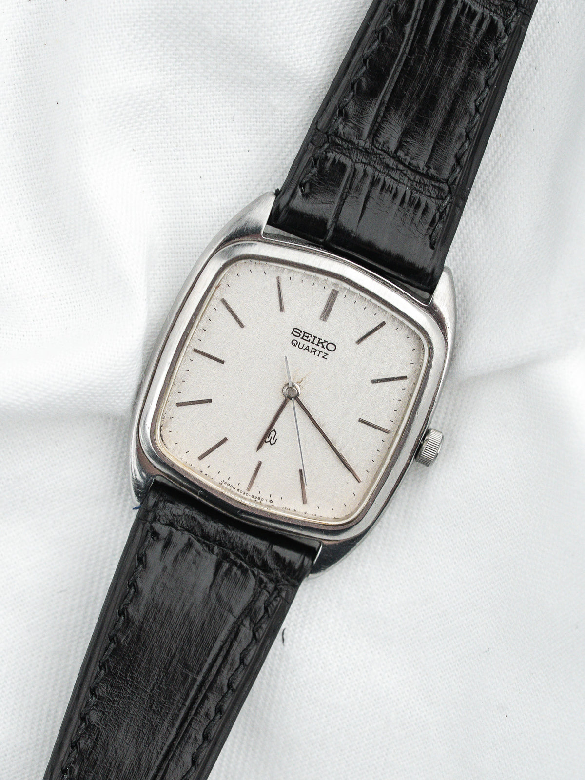 Seiko Quartz vintage watch with silver dial, black leather strap, square case on white background