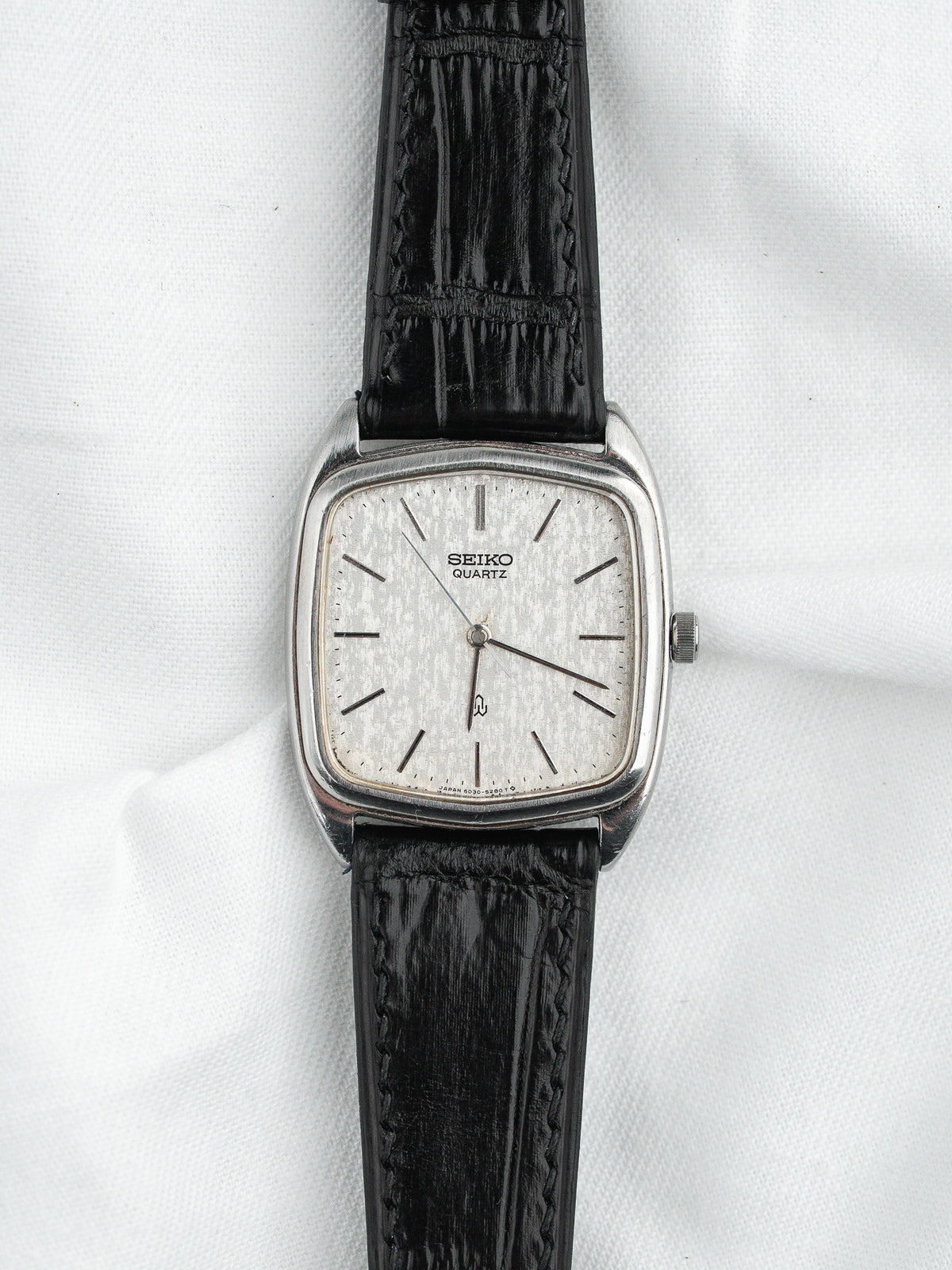 Vintage Seiko Quartz watch with silver dial, black leather strap, square case on white background
