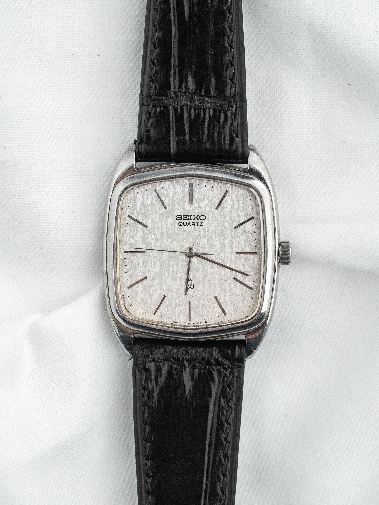 Seiko Quartz vintage watch with silver dial, black leather strap, square case on white background