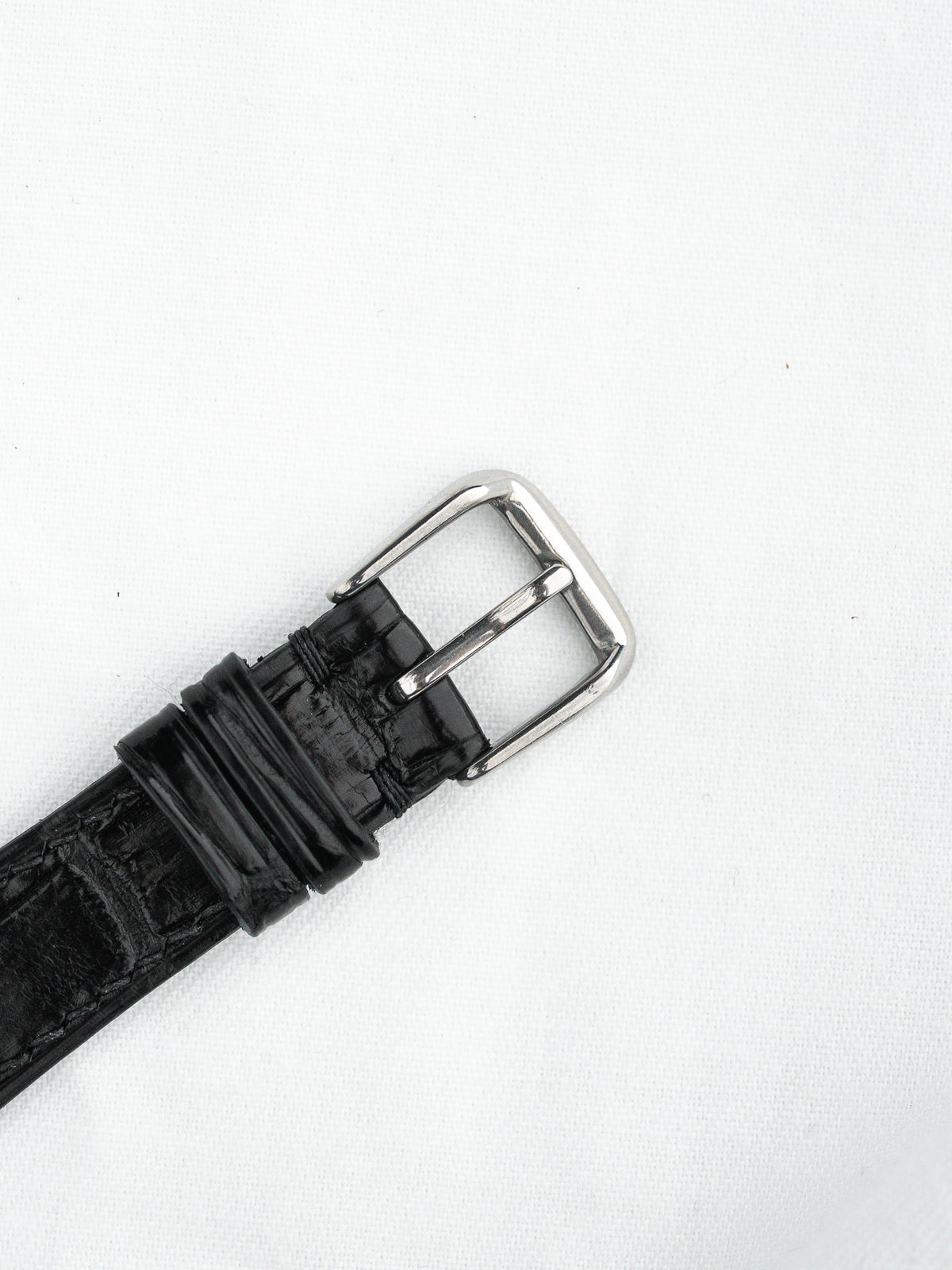 Black alligator leather watch strap with polished silver buckle on white background