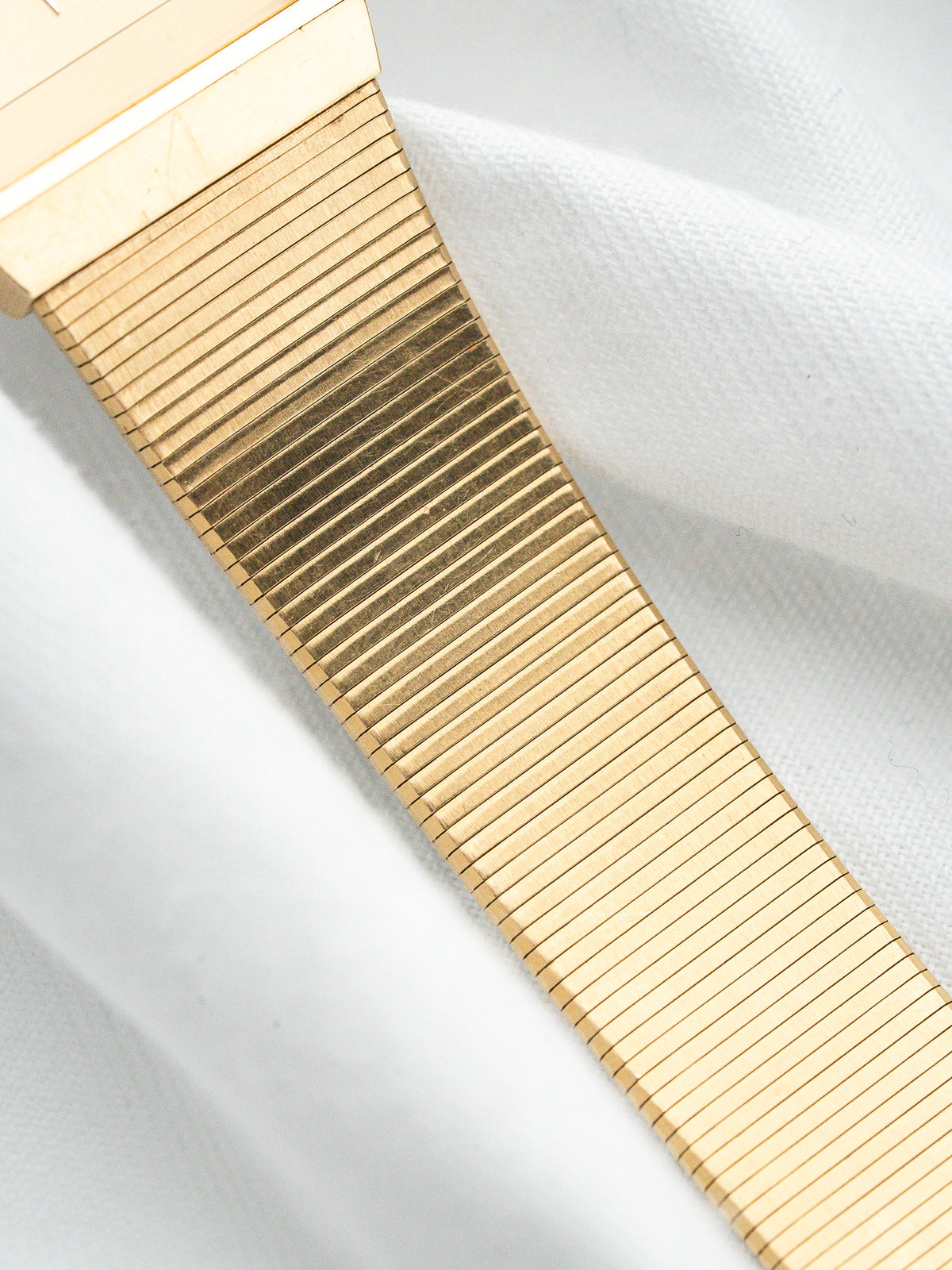 Vintage gold watch bracelet with ribbed design on white fabric