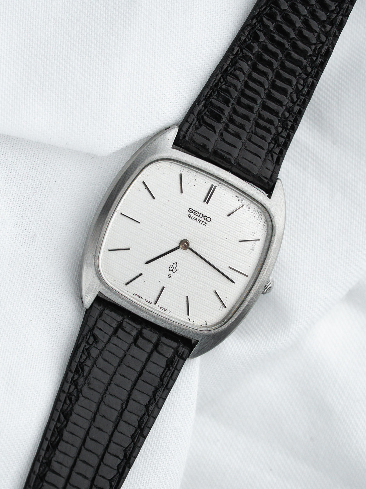 Seiko Quartz vintage watch with silver dial, black lizard strap, on white fabric