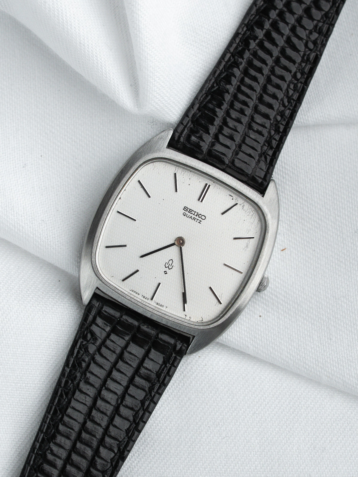 Seiko Quartz vintage watch with silver case, white dial, black textured strap on white fabric