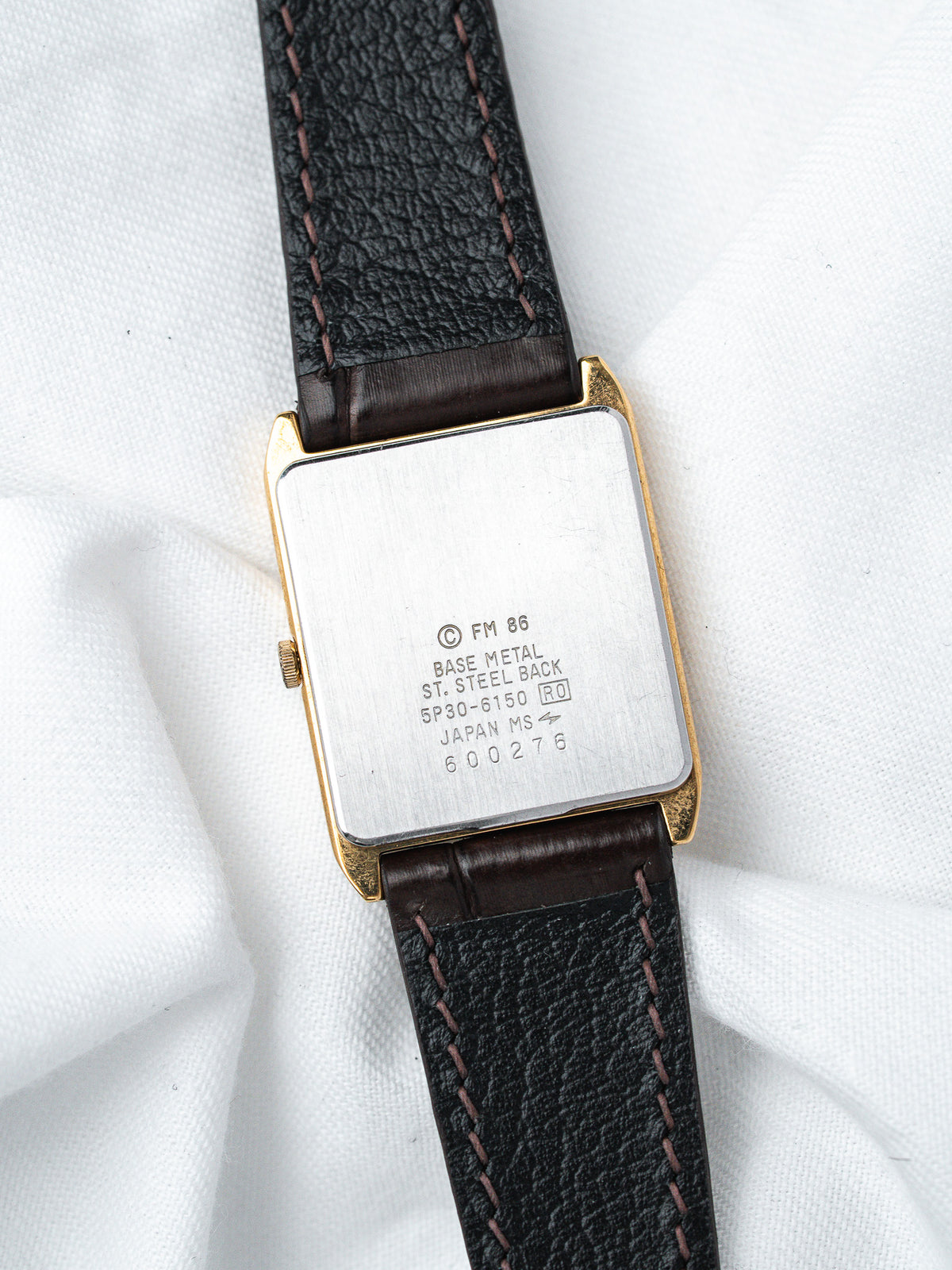 Vintage watch with gold case, black leather strap, and engraved steel back