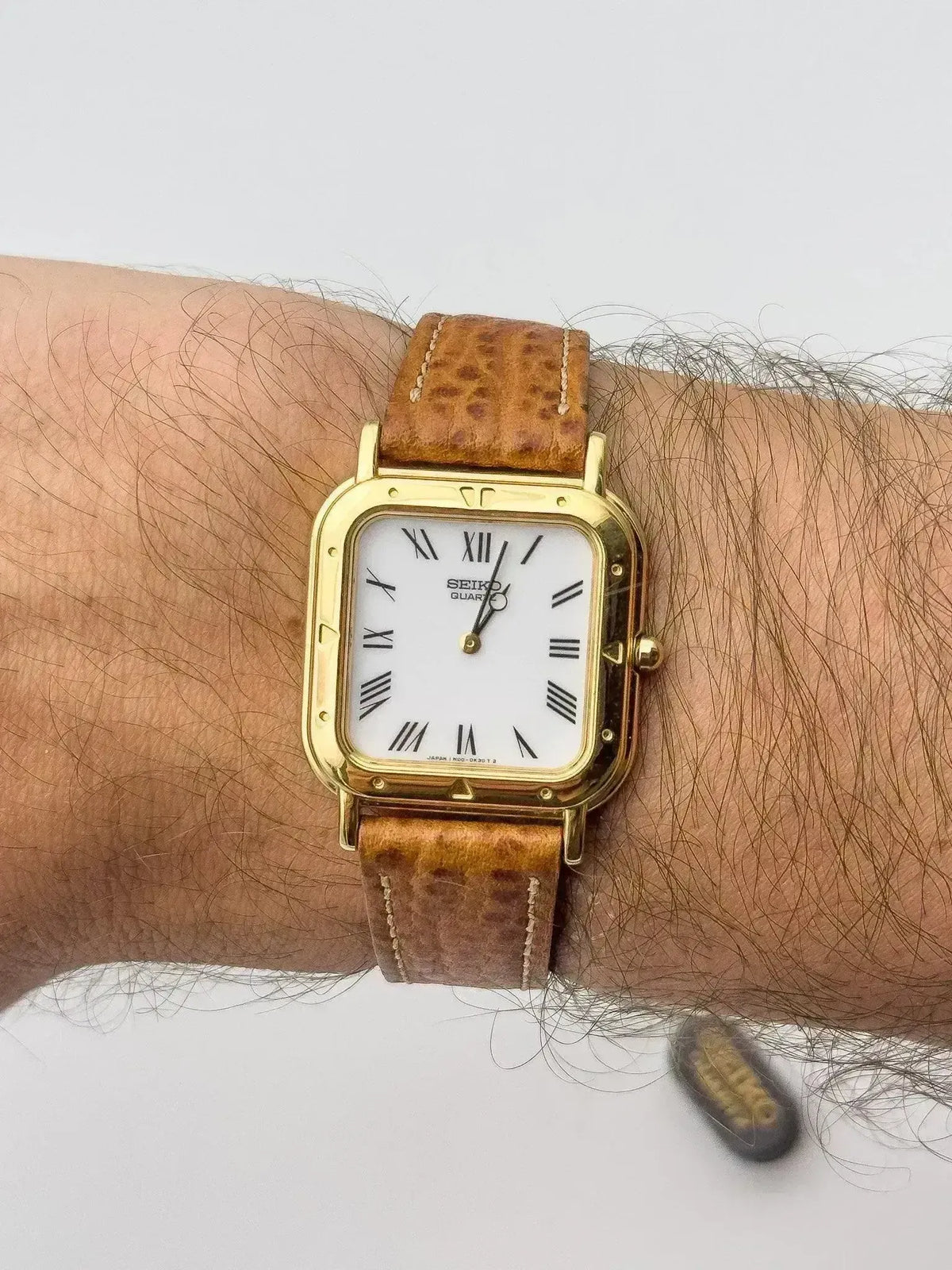 Seiko vintage watch with gold case, white dial, Roman numerals, brown leather strap on wrist