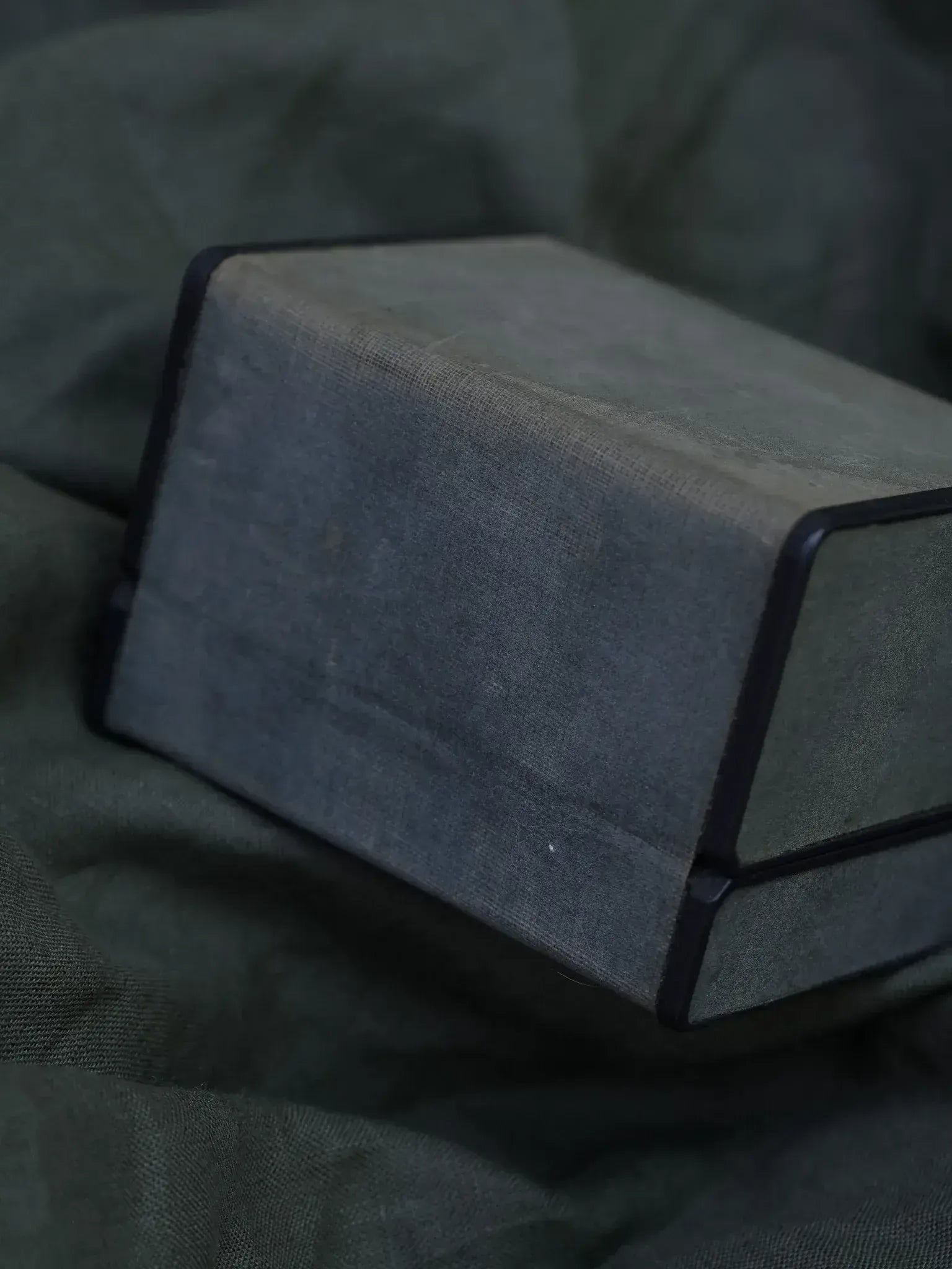 Vintage fabric-covered box with black trim, resting on olive green cloth
