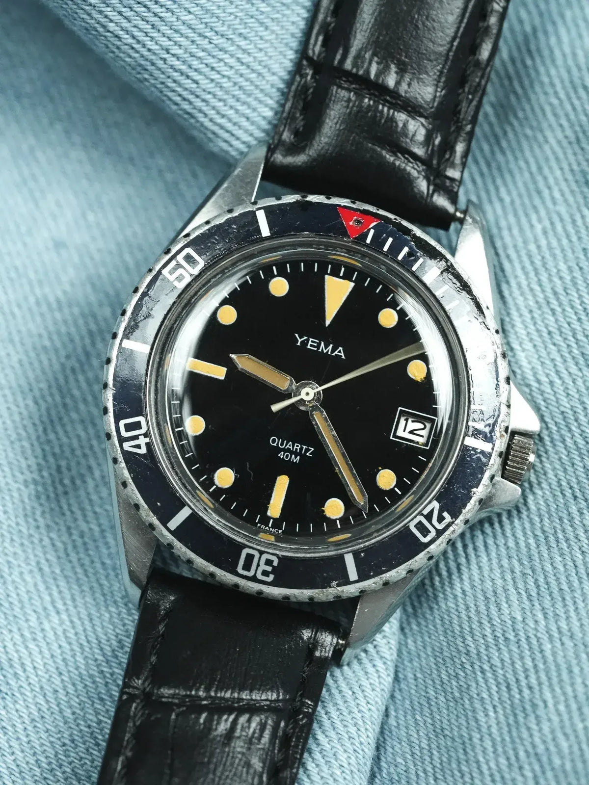 Vintage Yema diver watch with black dial, luminous markers, and black leather strap on denim