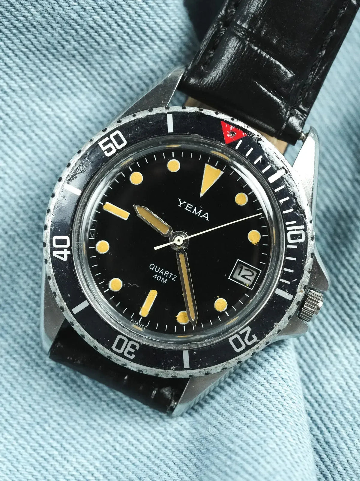 Vintage Yema diver watch with black dial, yellow markers, and black leather strap on denim