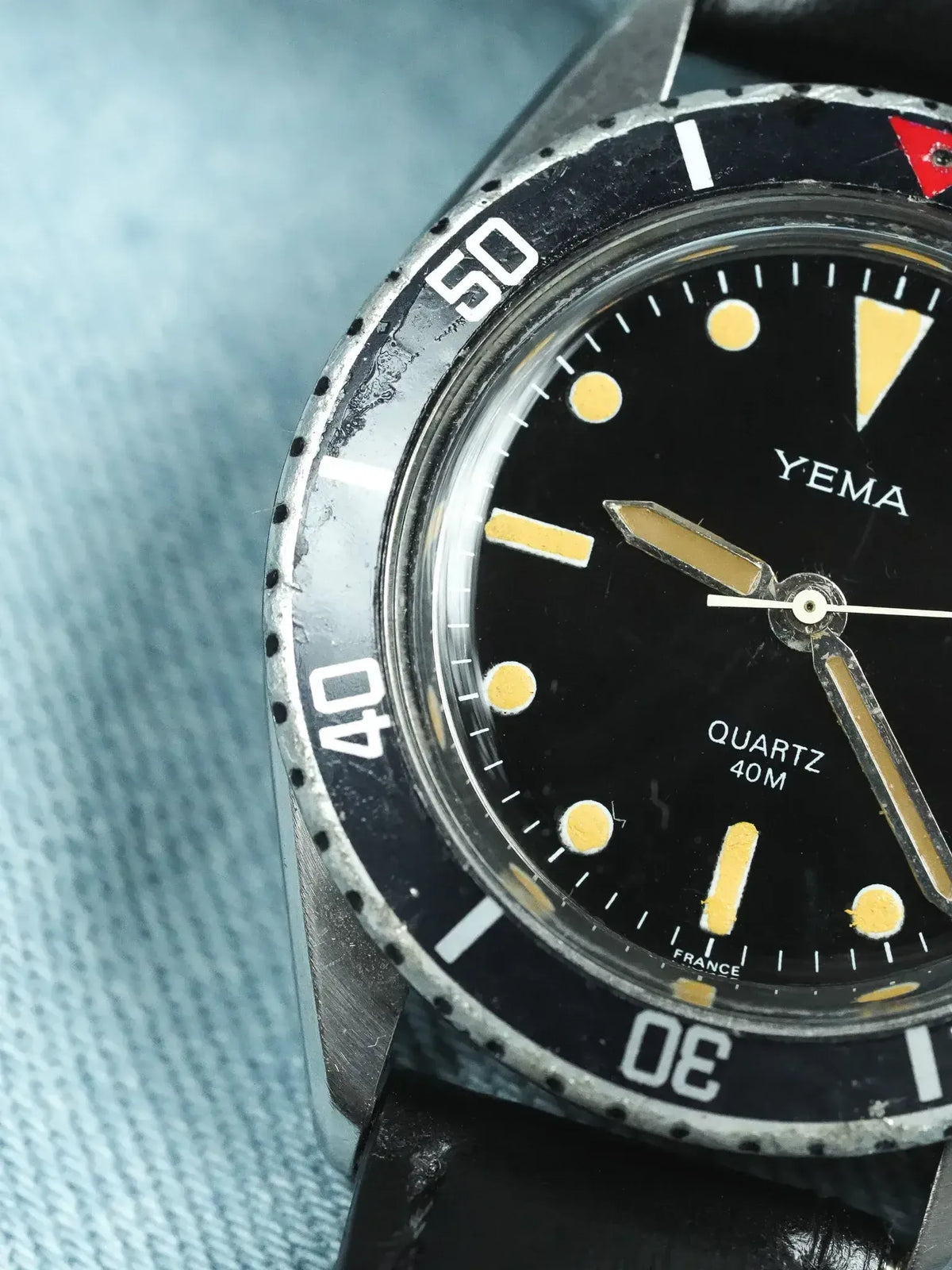 Vintage Yema diver watch with black dial, luminous markers, and rotating bezel on denim