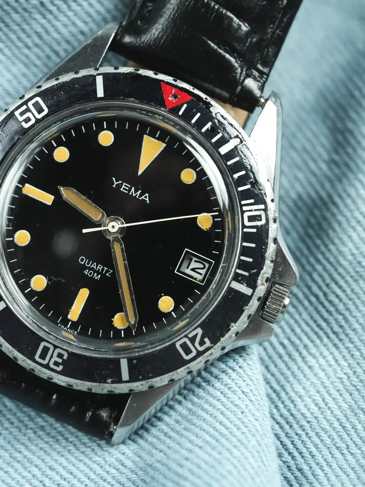 Vintage Yema diver watch with black dial, yellow markers, and black leather strap on denim