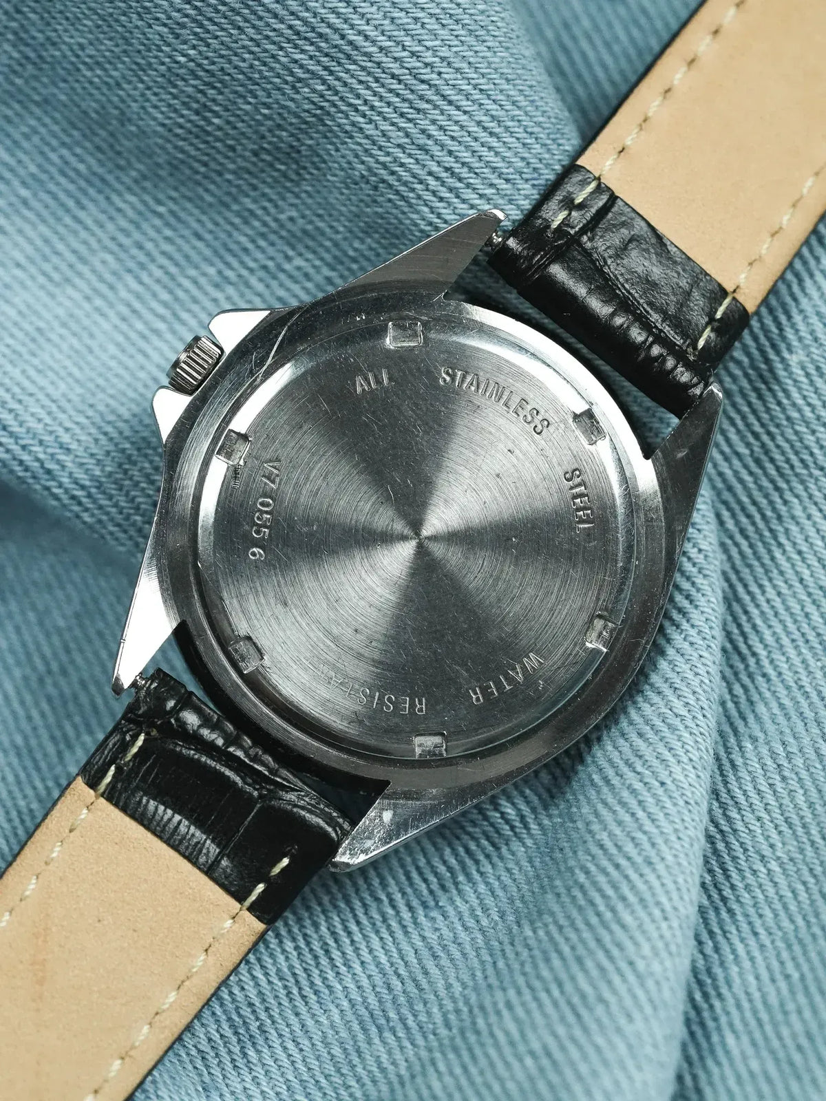 Stainless steel watch back with engraved text, black leather strap on denim
