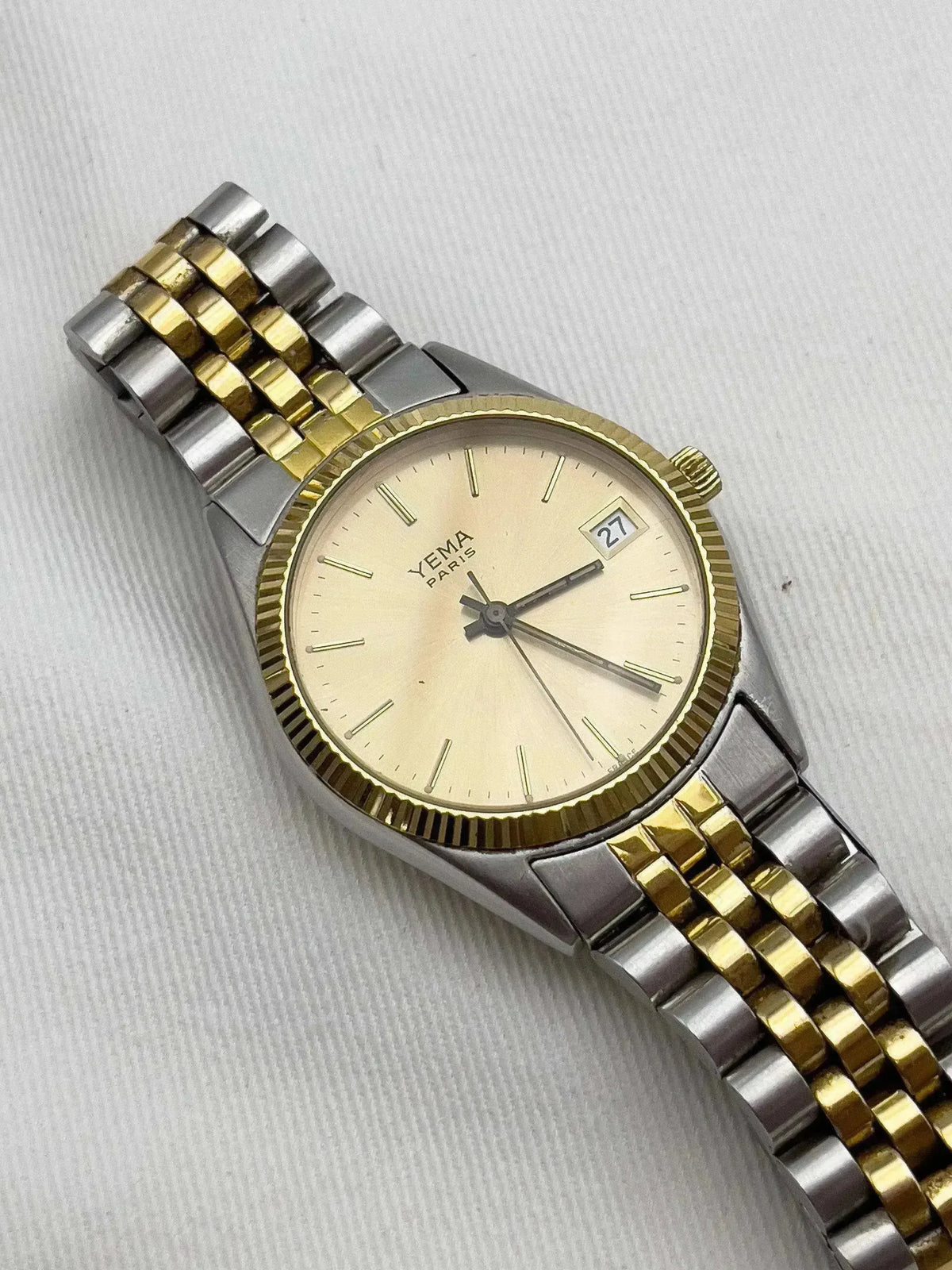 Yema Paris vintage watch with gold and steel bracelet, cream dial, date window, on textured background
