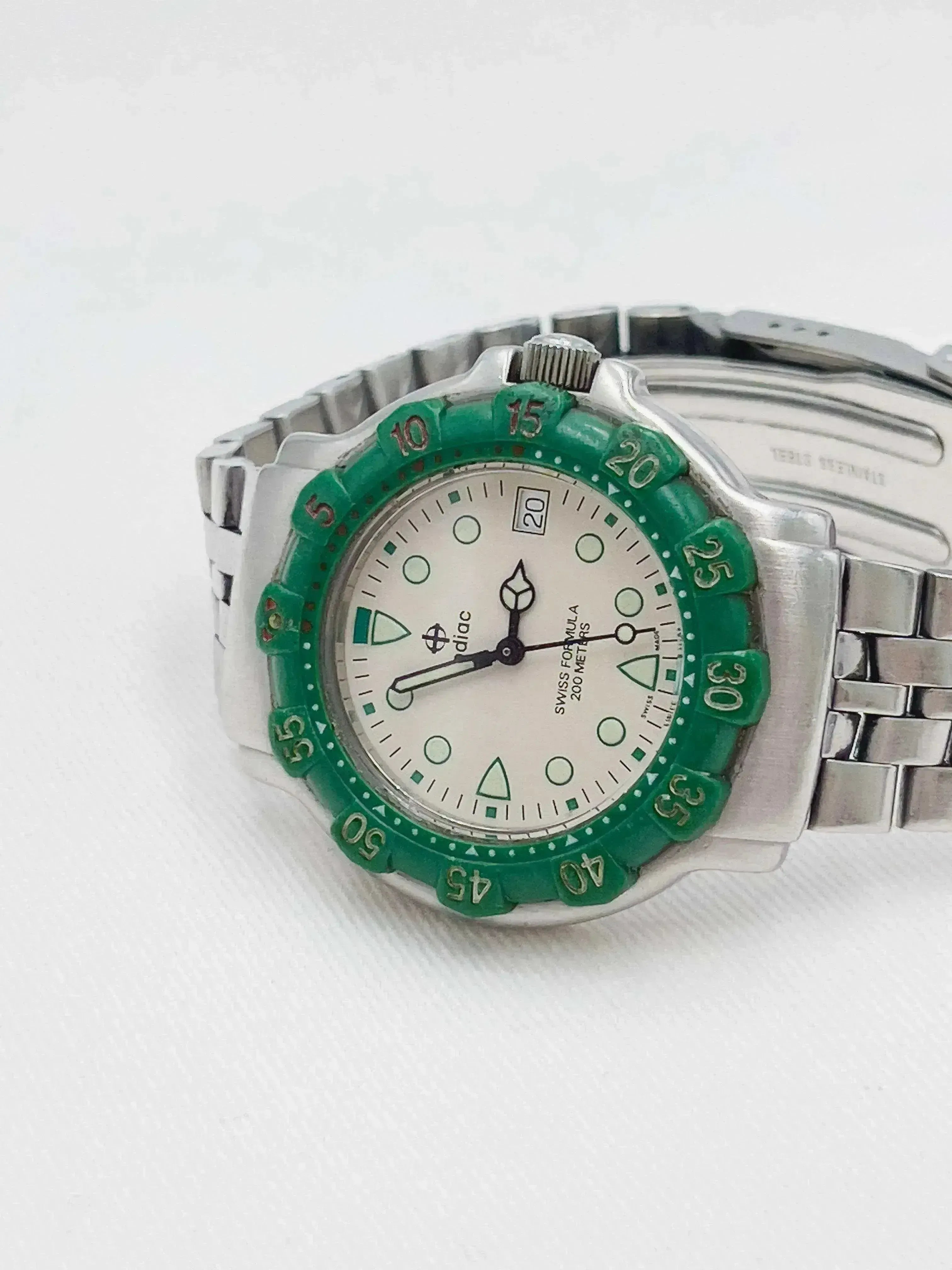 Diac vintage watch with green bezel, white dial, and stainless steel bracelet on white background