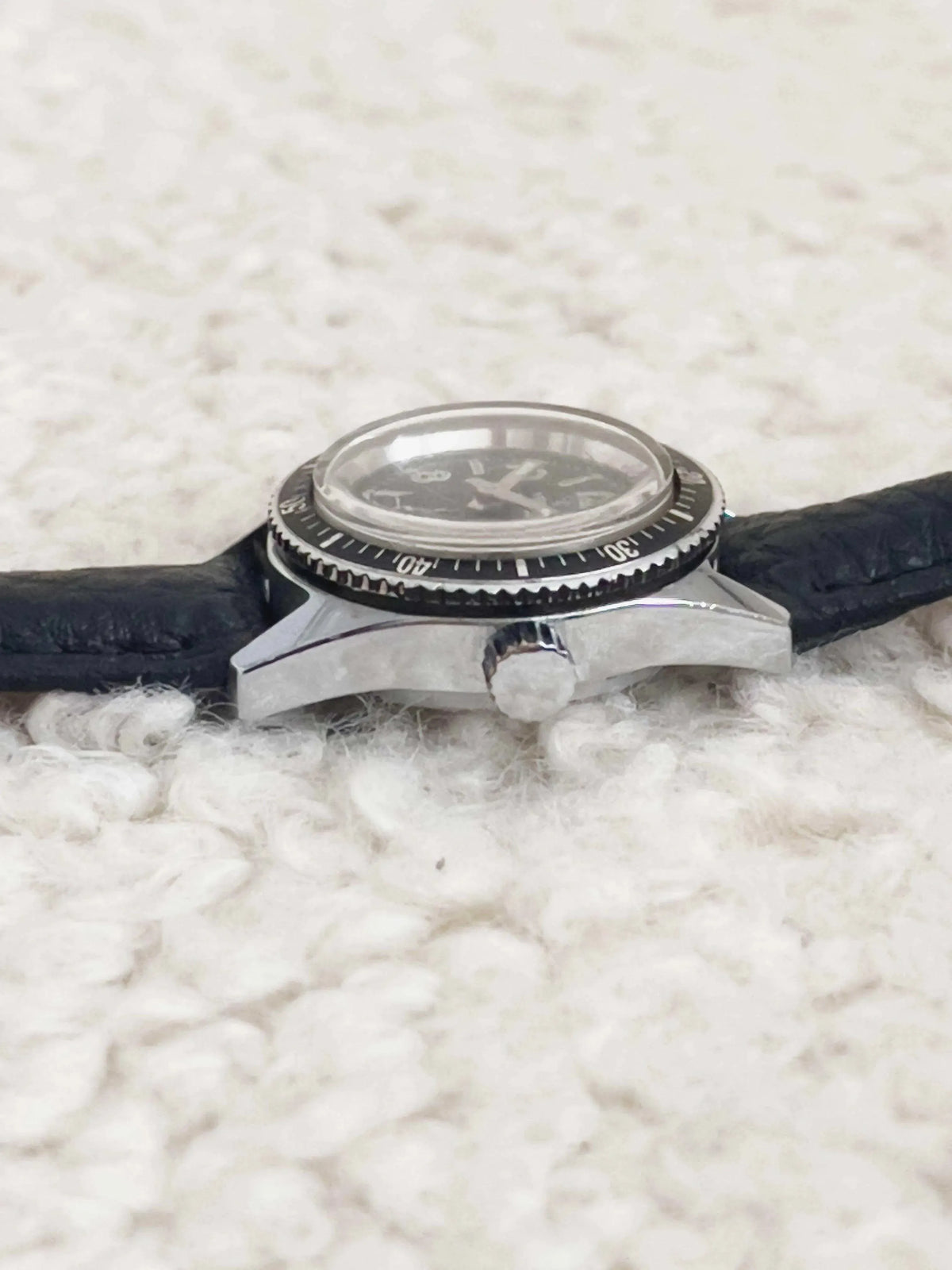 Vintage Omega Seamaster diver watch with black bezel, silver case, and black strap on textured surface